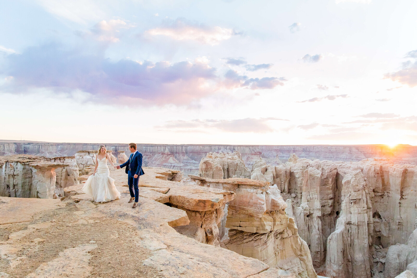 bride and groom hold hands at the grand canyon as they walk toward their destination wedding photographer