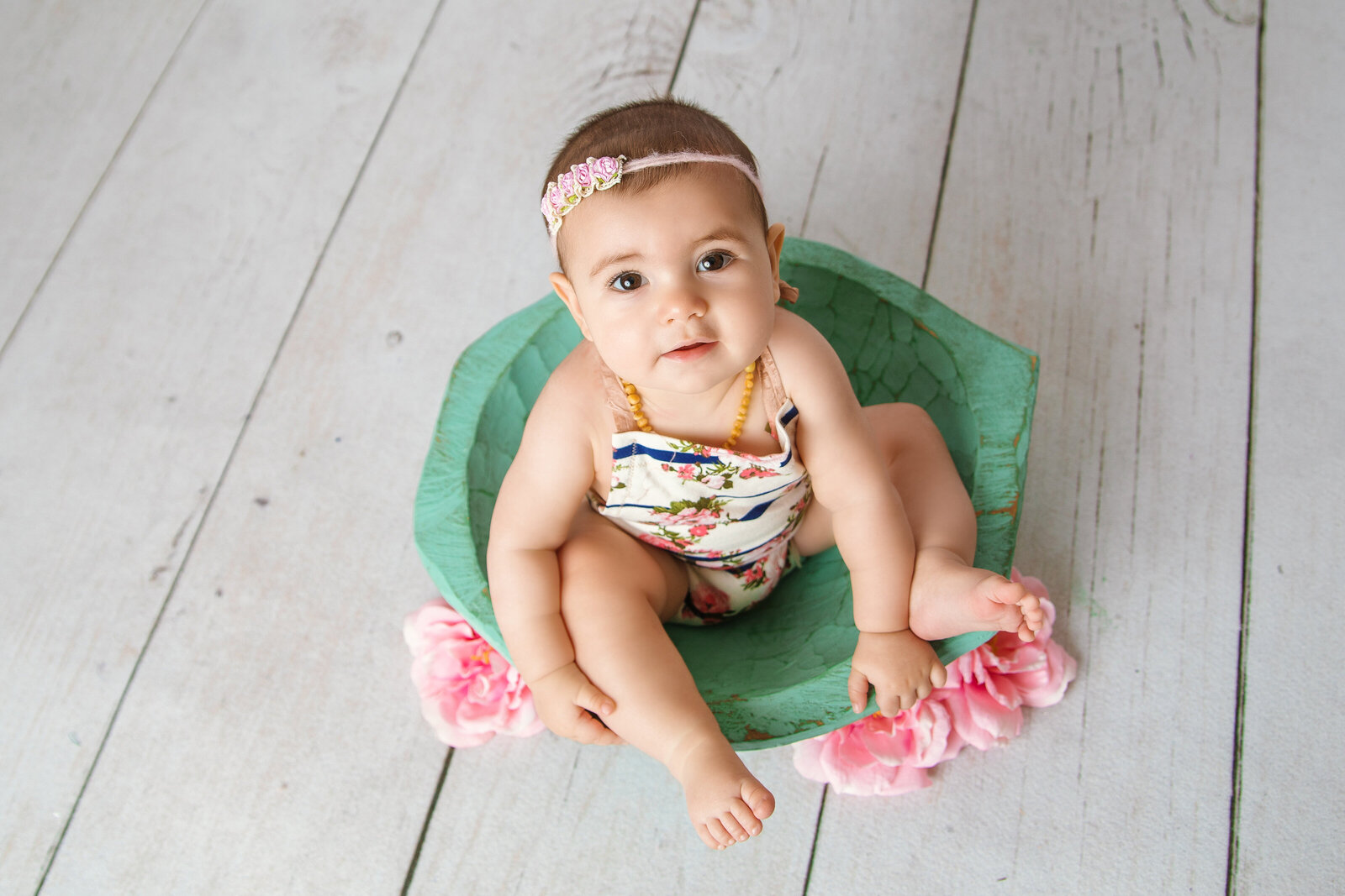 Milestone Photographer, a baby sits on a sea foam colored wooden bowl with flowers beside it