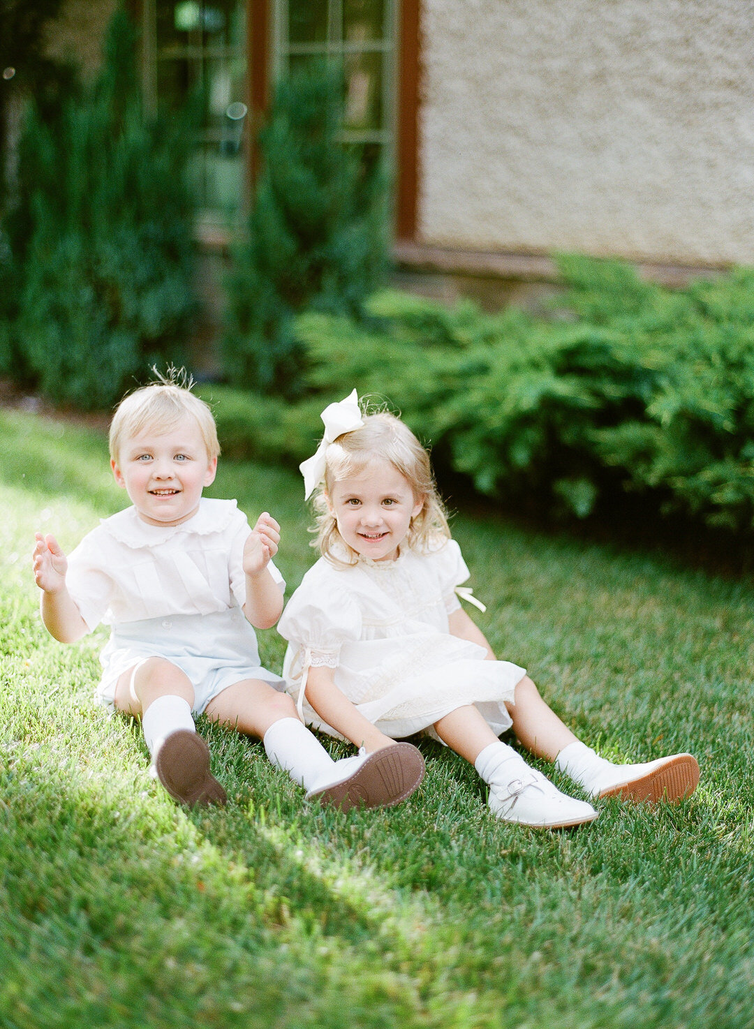 flower girl and ring bearer sitting in grass smiling