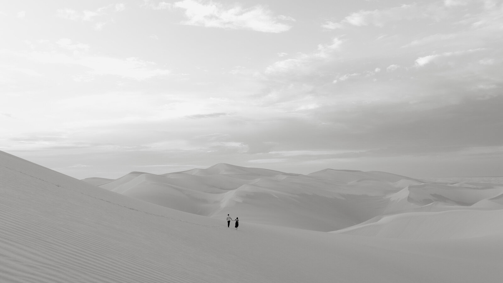 A couple walking through vast desert dunes, captured in an artistic and cinematic wedding photography style, perfect for destination weddings.