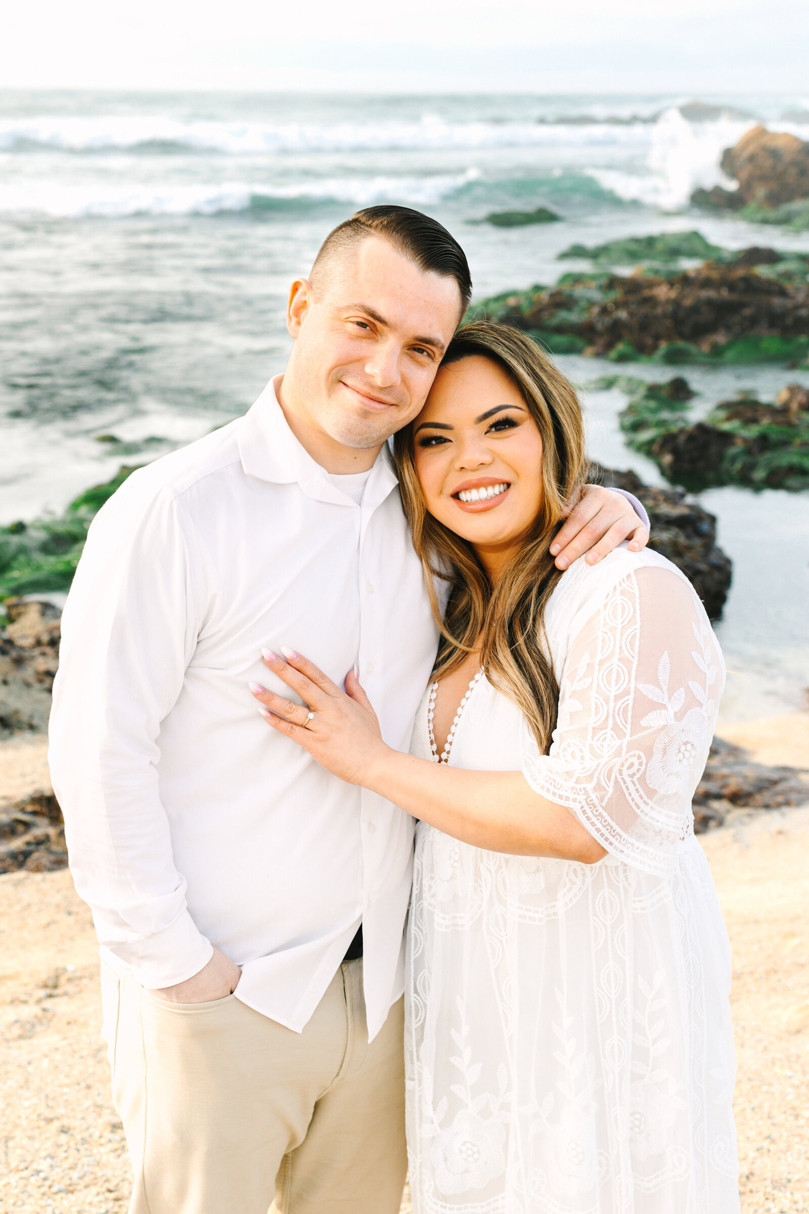 An engaged man and woman take photos on the beach in Pacific Grove, Monterey, California near Big Sur.