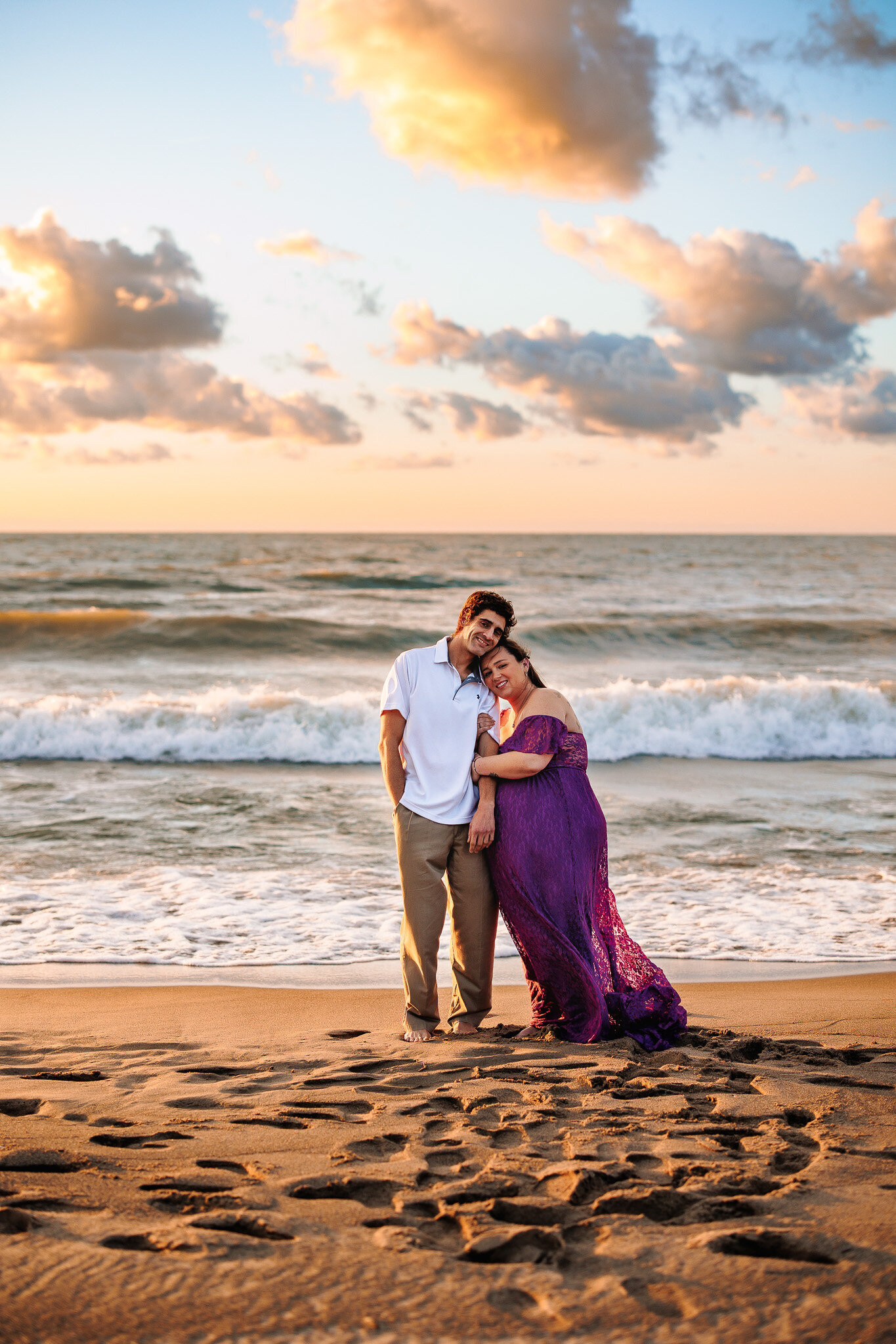 Couple snuggles in front of the water on a beach with a gorgeous golden sunset in the background 