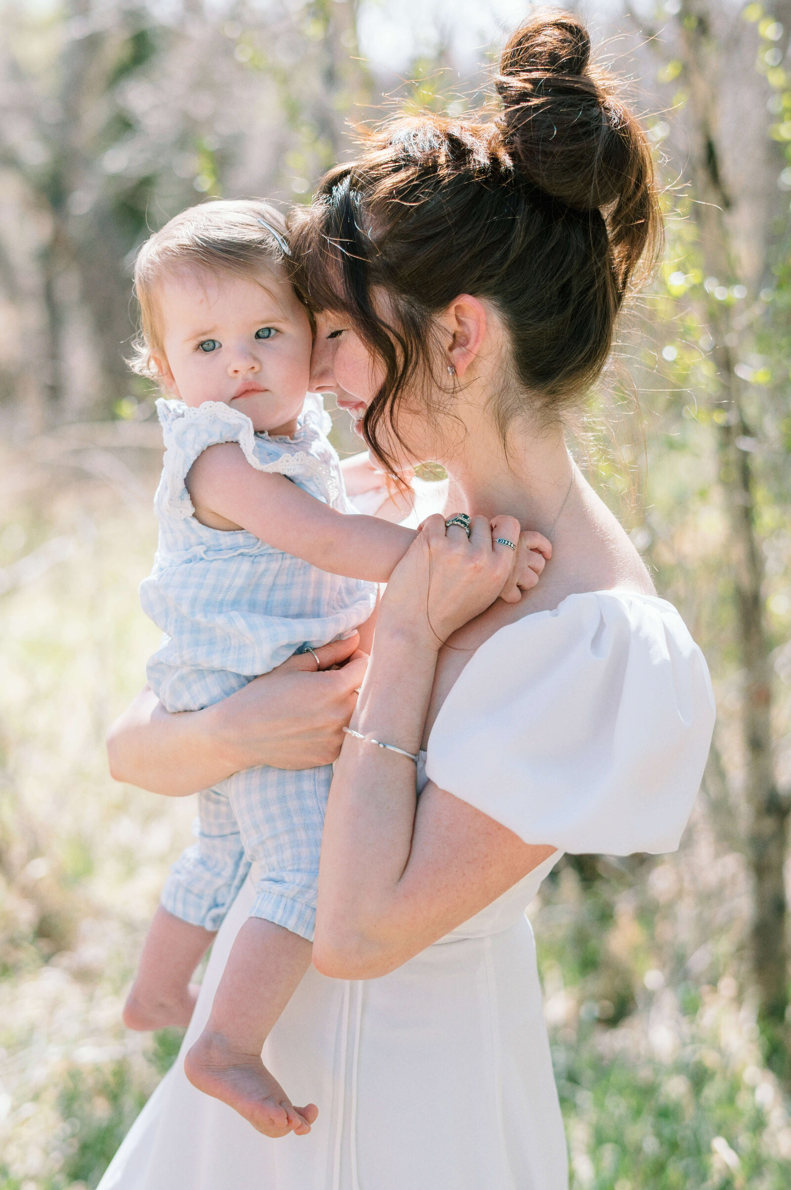 A woman in a white dress hugs her young baby who is dressed in a light blue outfit