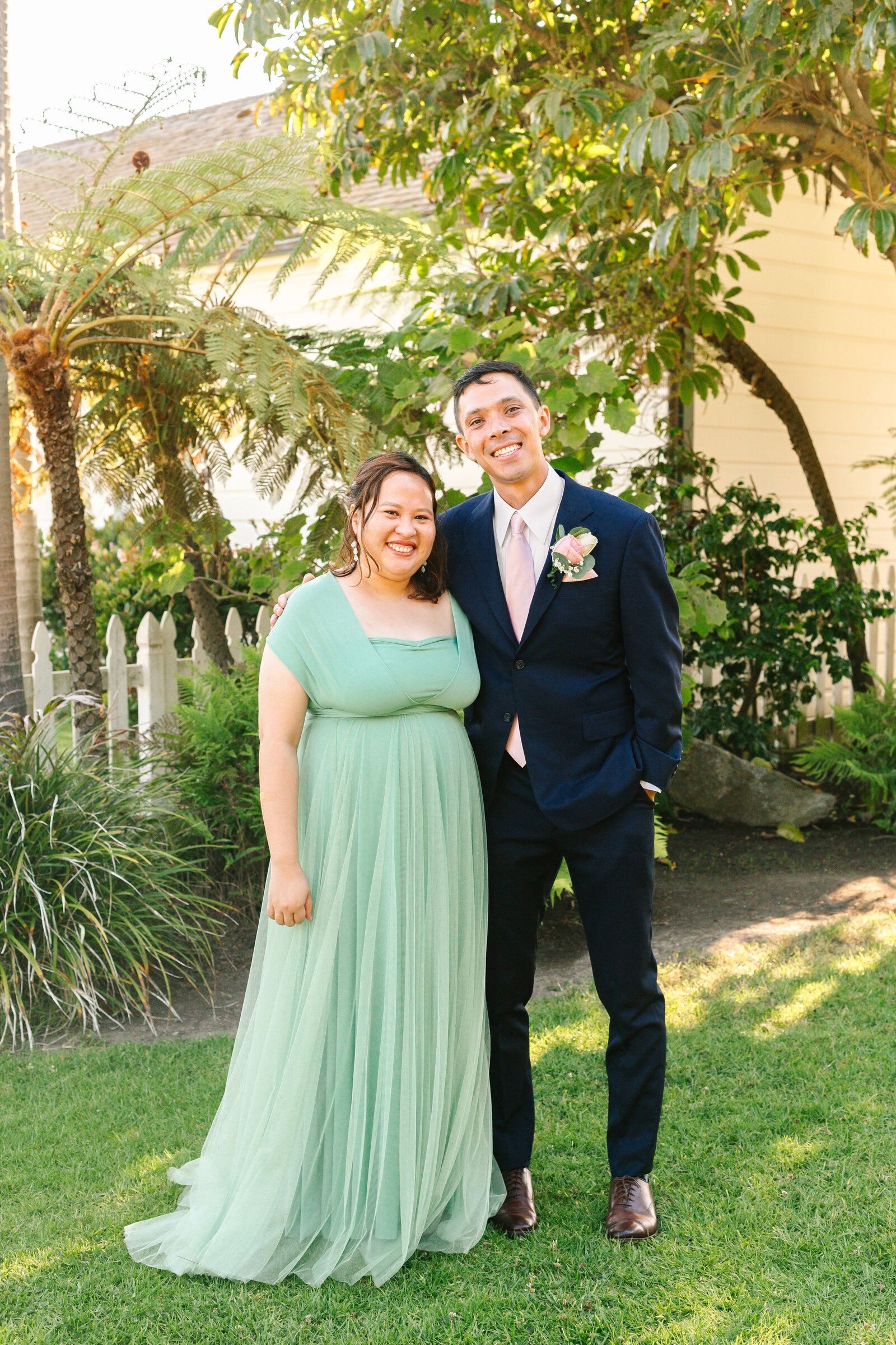 A groom poses with a bridesmaid in a teal maxi dress.