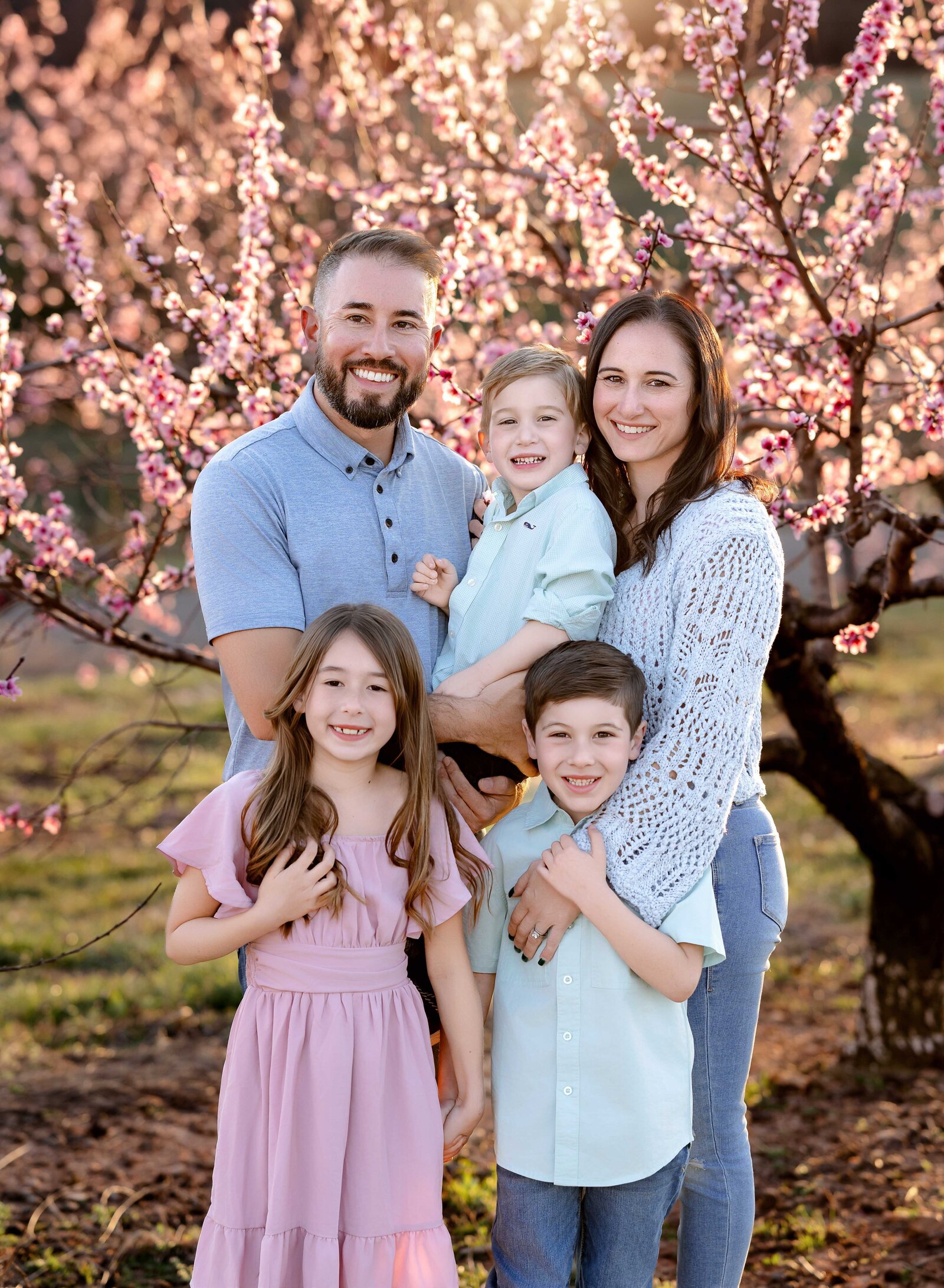Family hugging each other  in peach orchard field. Family photo taken by Jenni Nikki Photography near Atlanta, GA.