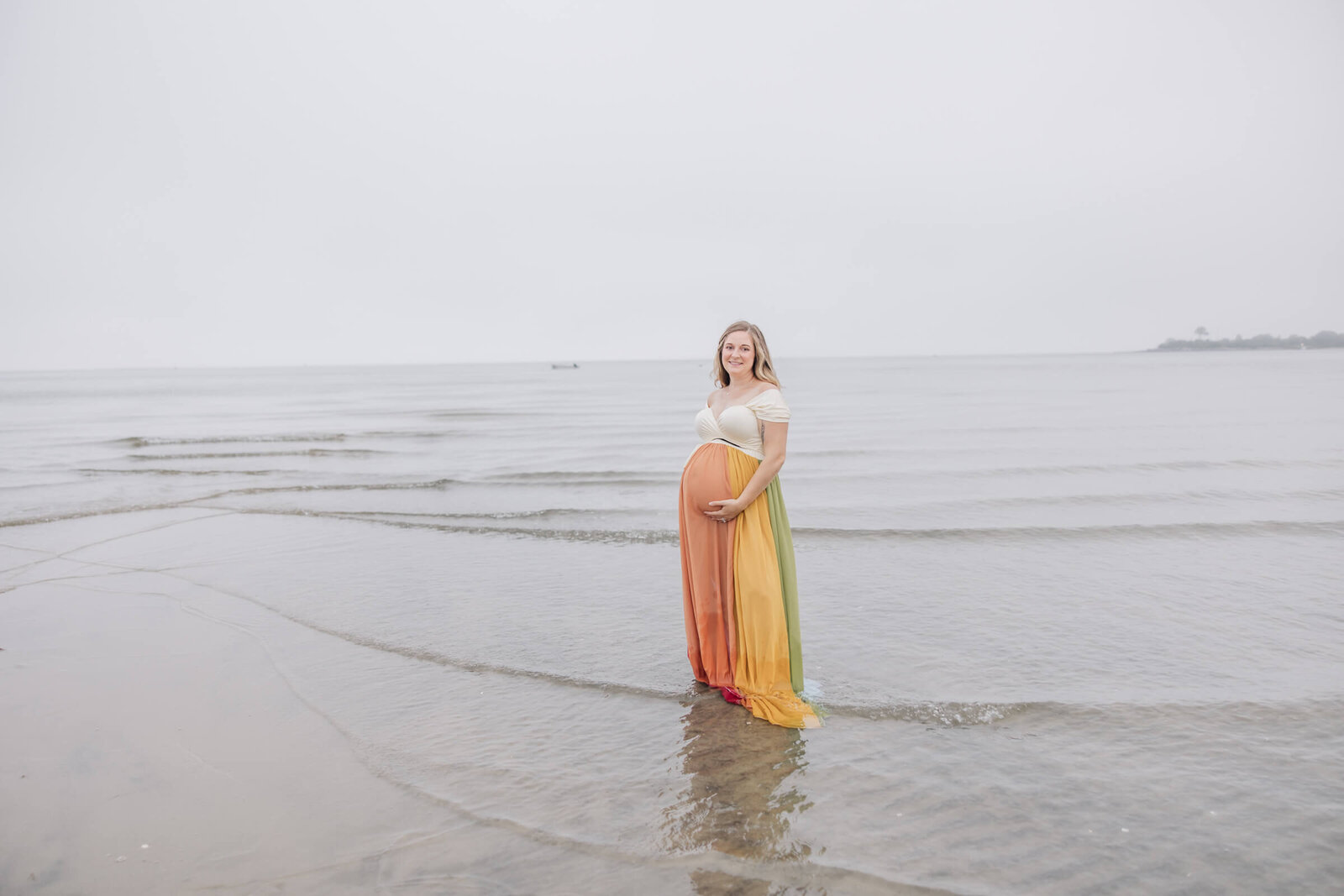 Mom in a rainbow dress looks at camera from water at low tide