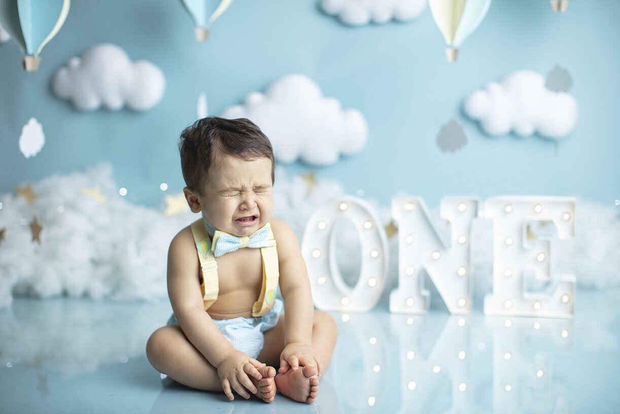 Baby boy crying at his hot air balloon cake smash.