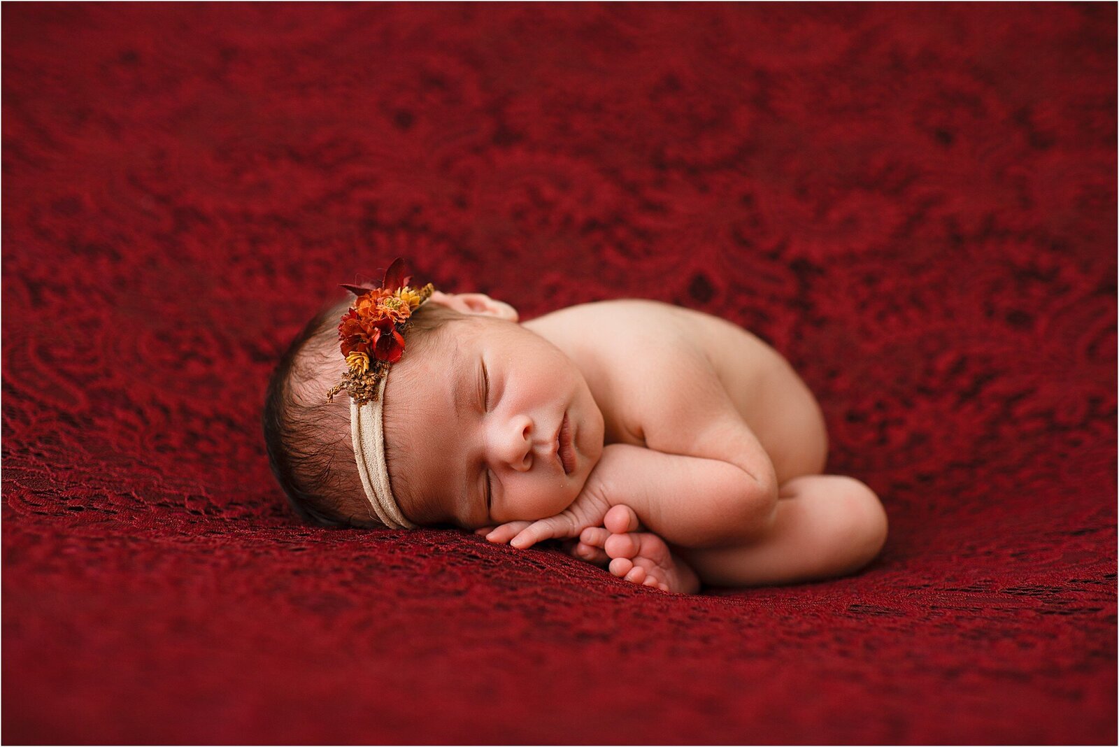 newborn baby on crimson lack blanket