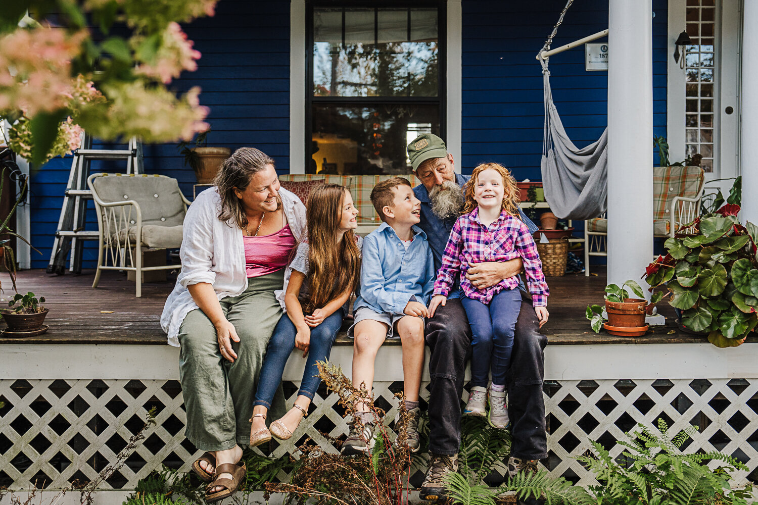 family with older kids sit on the porch of a blue victorian home