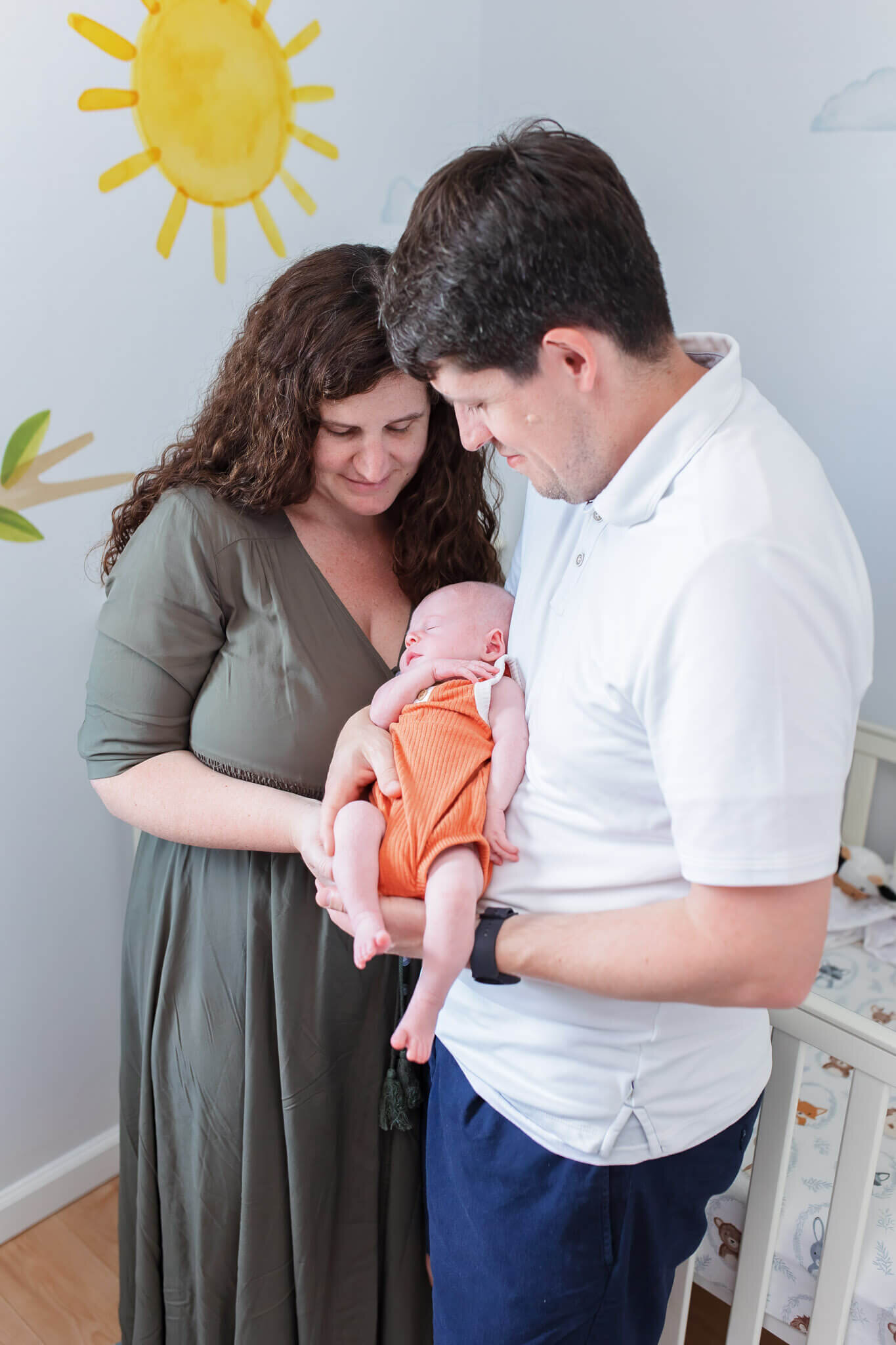 A mom and dad holding their newborn son and smiling down at him.