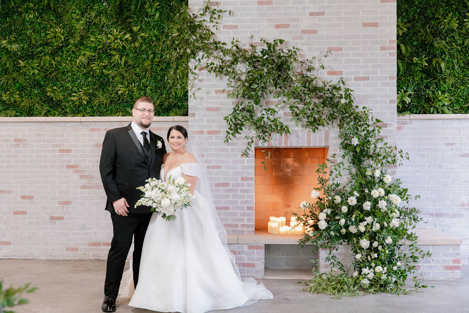 Bride and groom posing in front of a wall of candlelight and cascading floral arrangements at Grbic Events, a wedding venue in St. Louis.