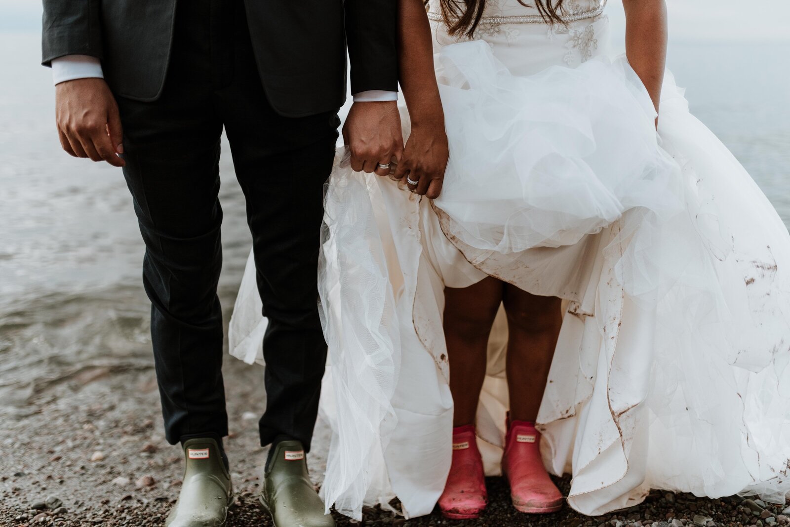 Newlywed couple showing their rubber boots and messy wedding clothes