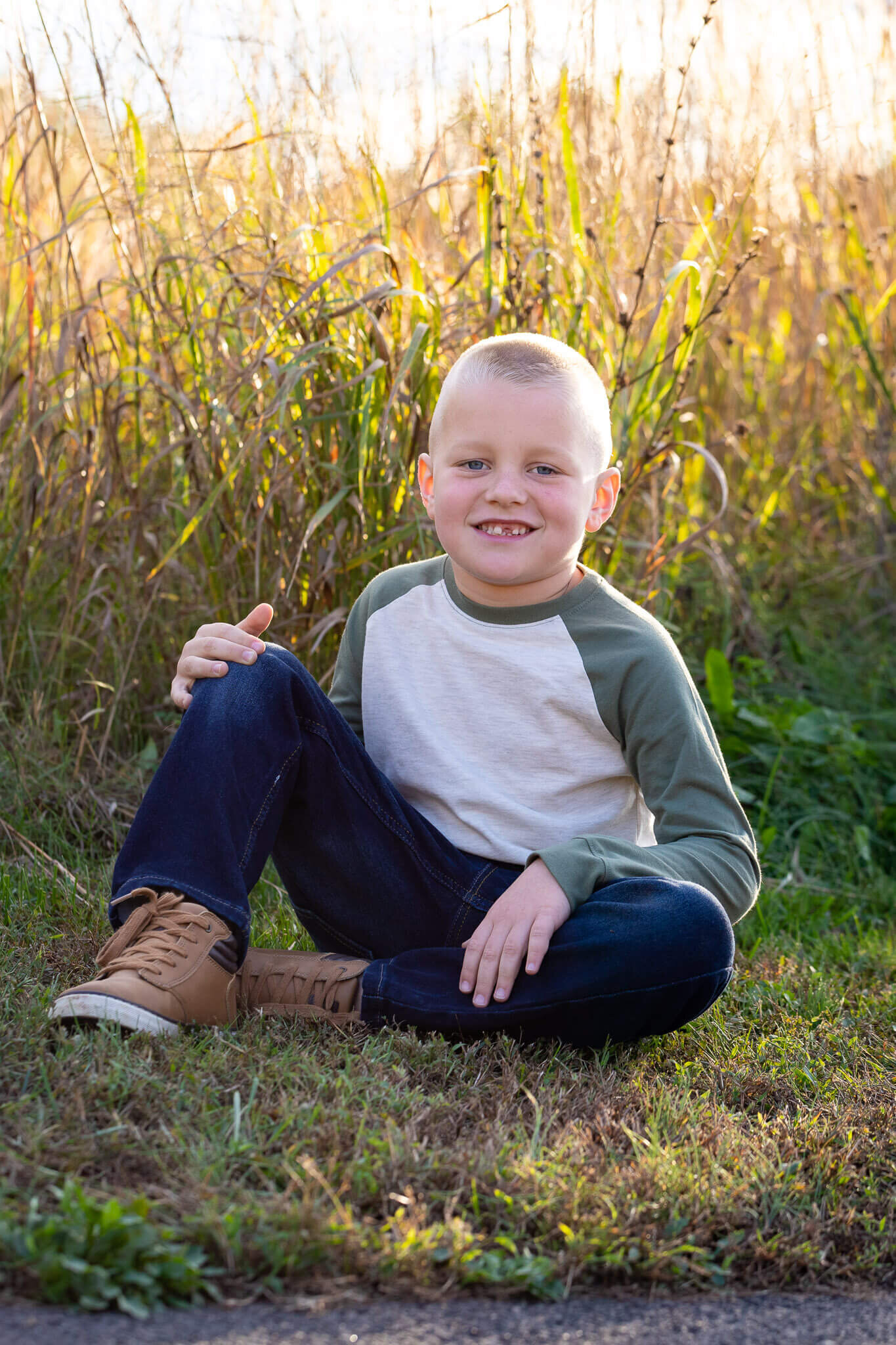 A boy sitting in the grass at a park at sunset.