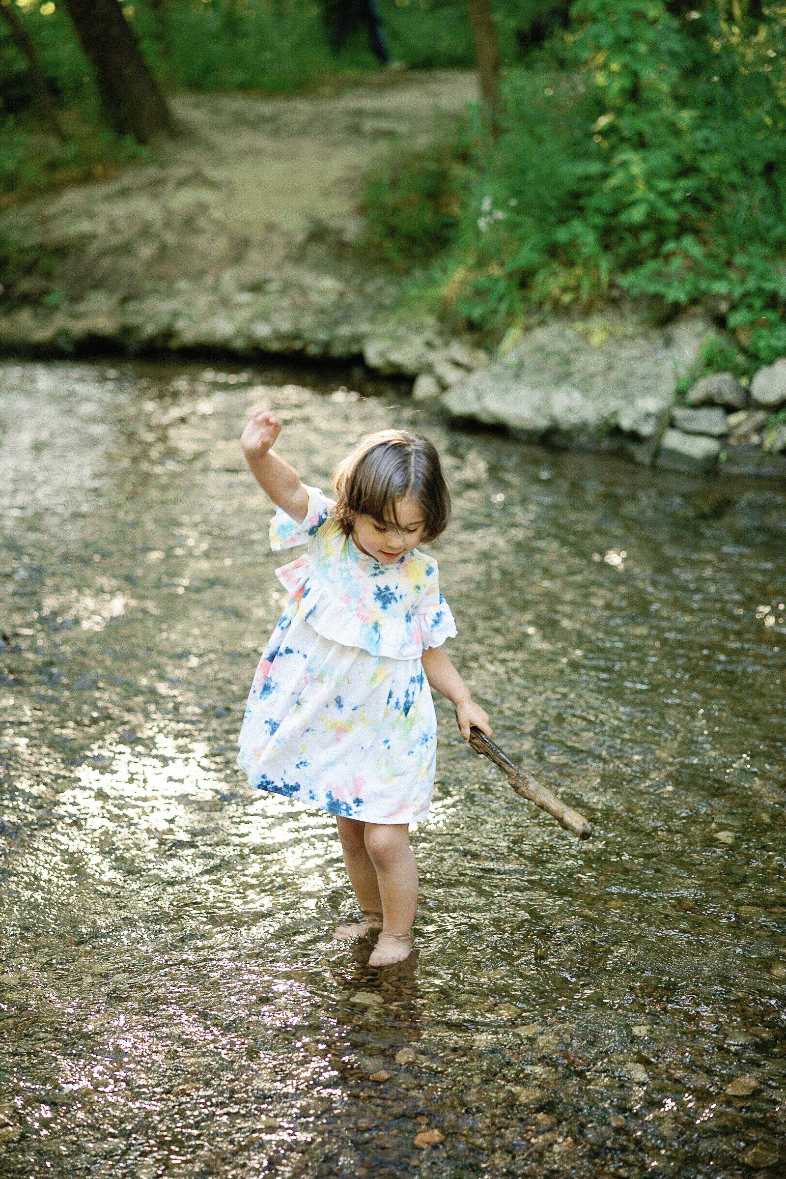 little girl walking barefoot through creek at Flowing Well Park in Carmel, Indiana