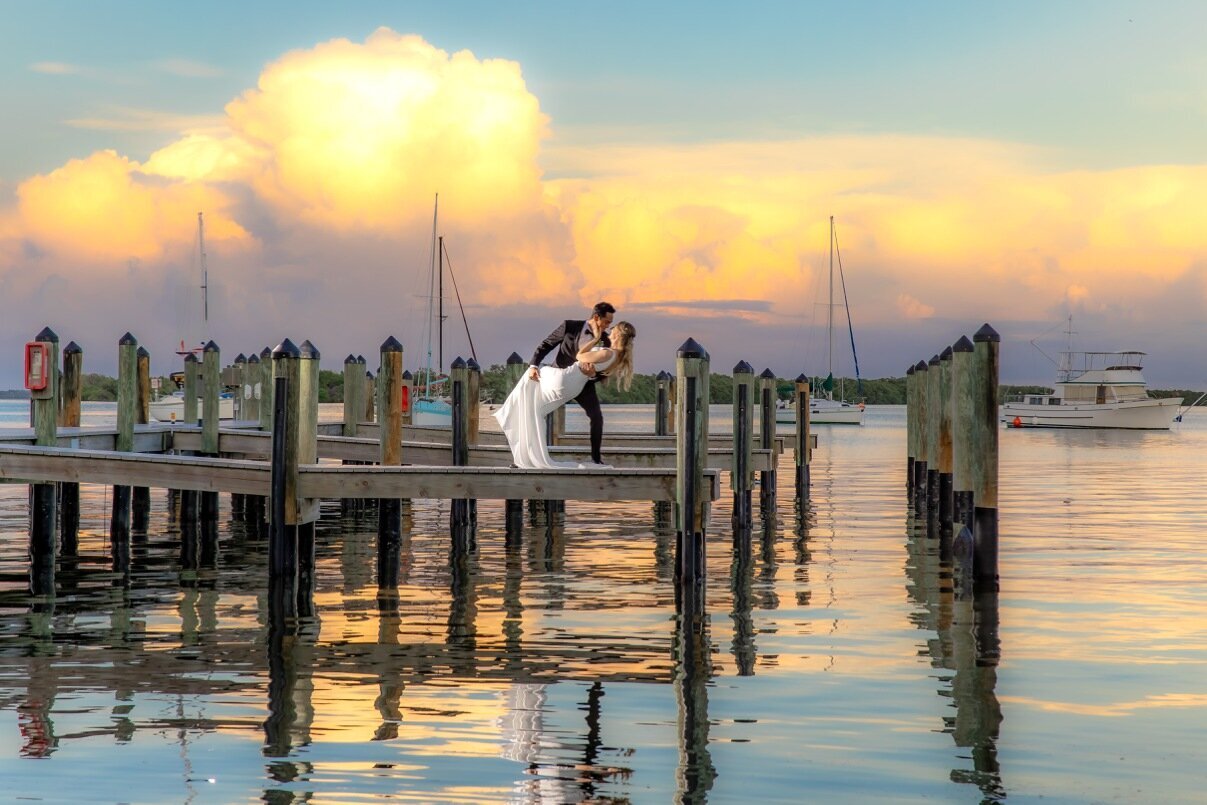 Beautiful wide angle portrait of groom dipping bride on the docks at Mar Vista with the sunset reflecting in the water