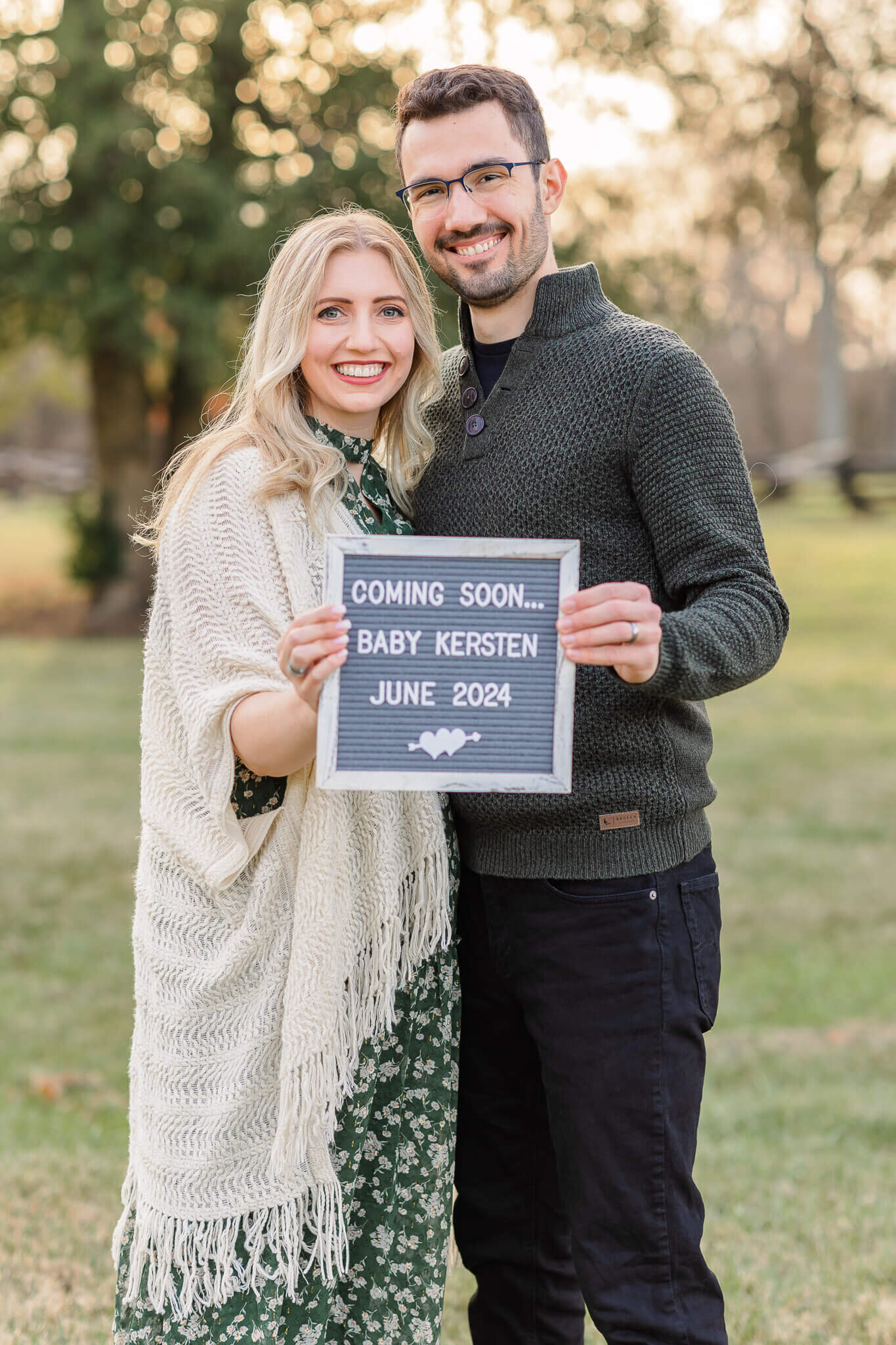 An expecting couple holding up a sign and smiling at the camera.