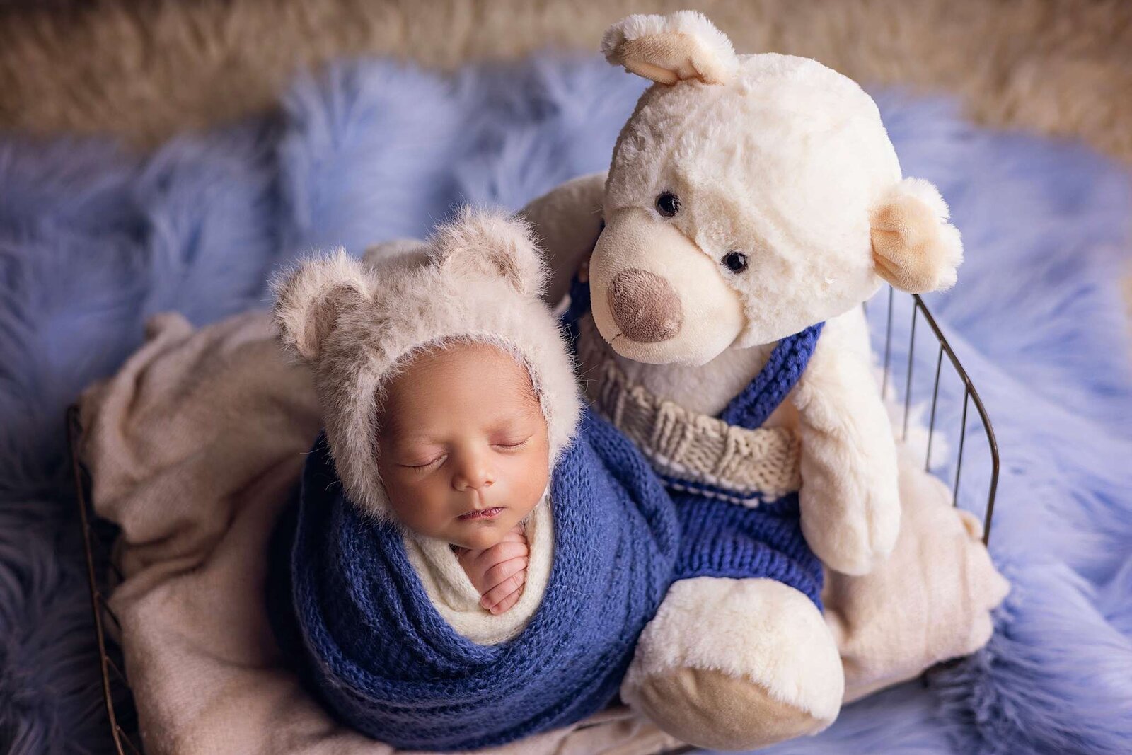 Newborn baby boy wrapped in a blue blanket, cuddling a teddy bear, captured by Bia Schaefer photography in Orlando.