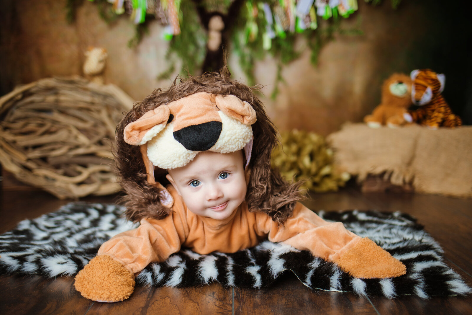 Milestone Photographer, a baby wears a lion costume and smiles in a jungle themed room
