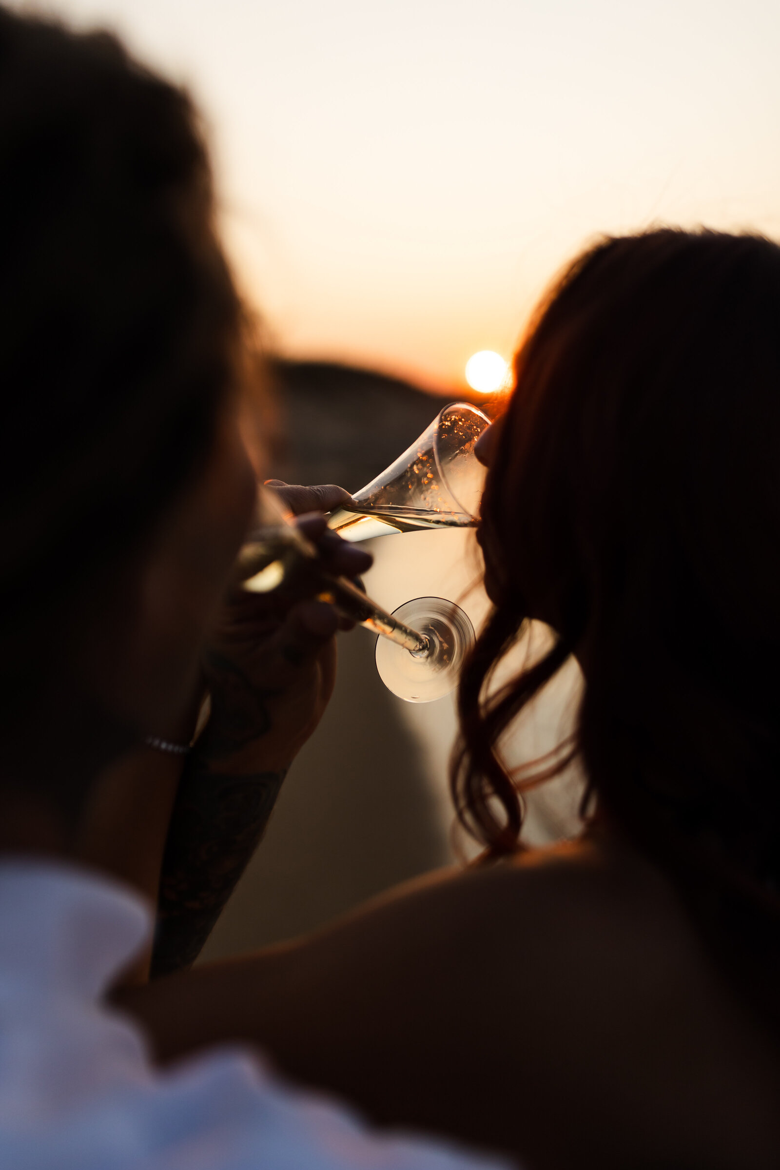 Bride and groom cross arms and sip champagne during engagement session on Plum Island, Massachusetts