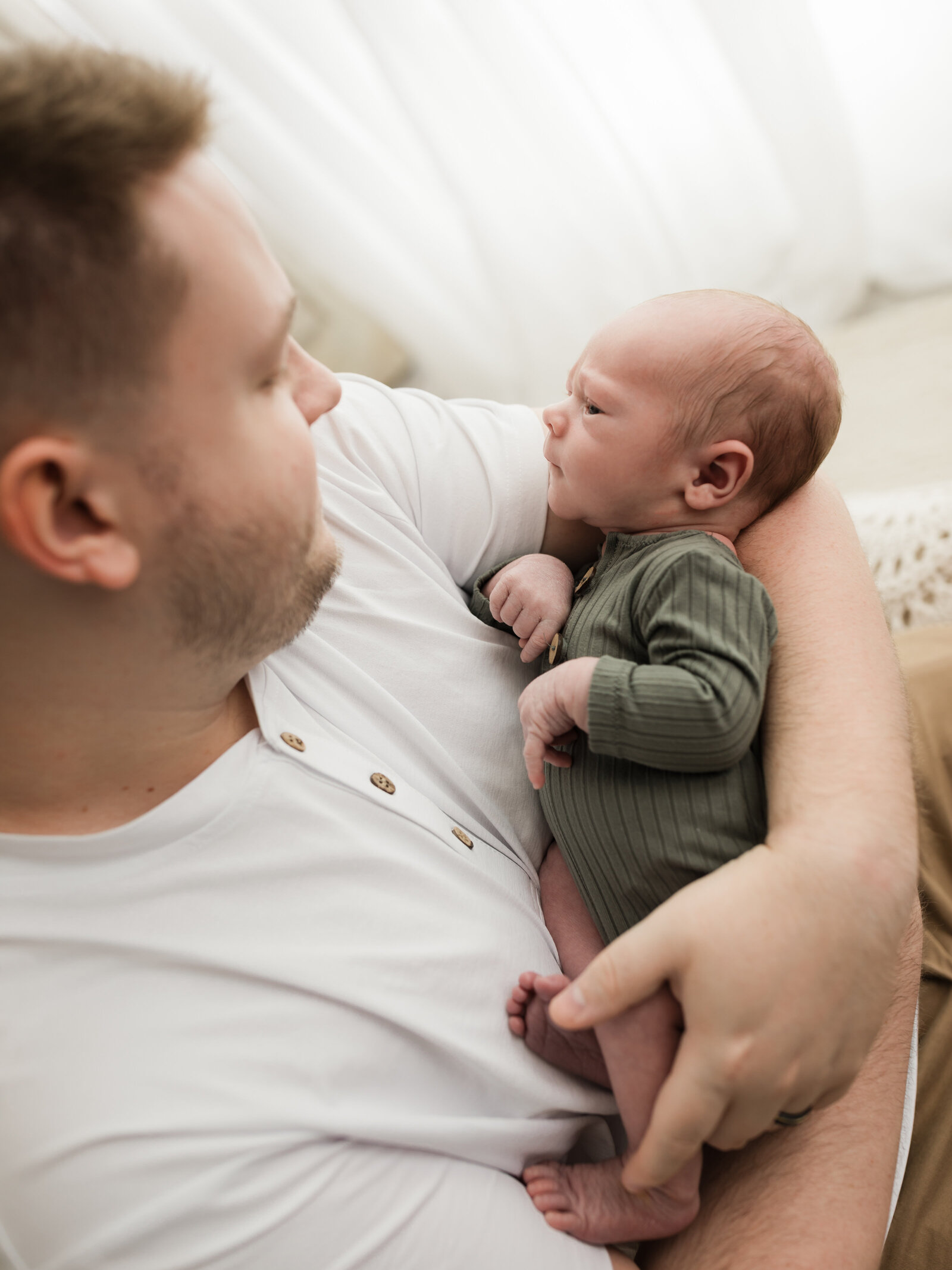 dad holding newborn baby boy in green onesie for studio newborn portraits