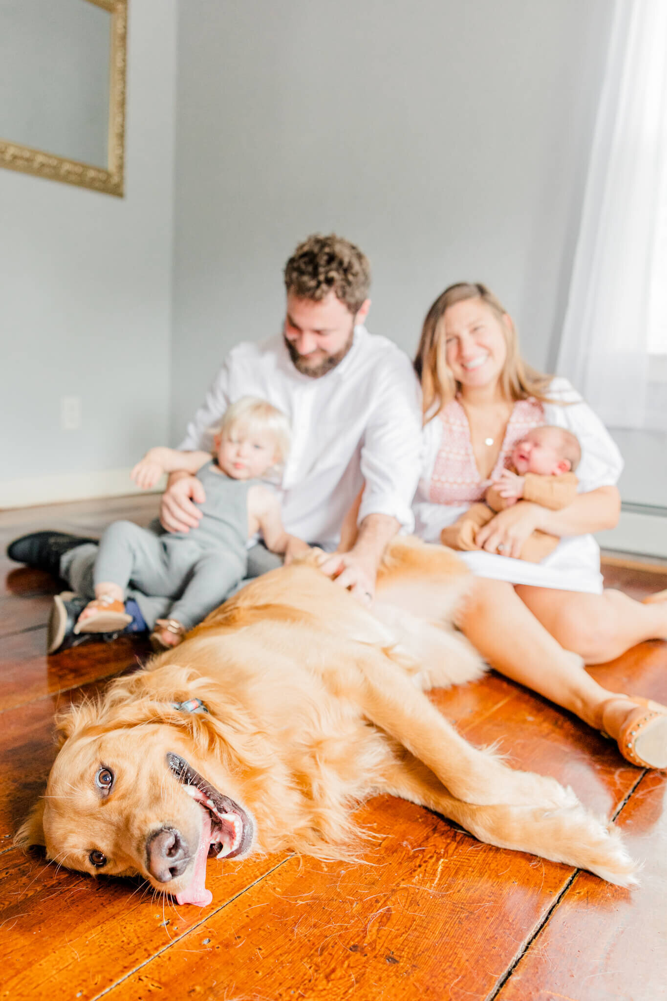 Dog lies down with his tongue out while family laughs in the background