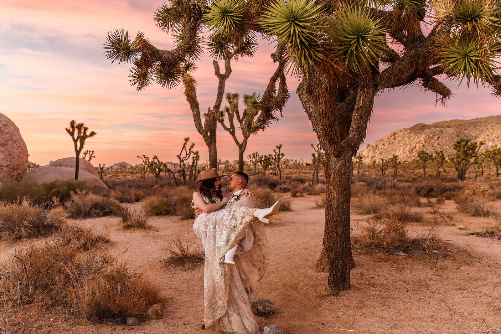 A groom carries his bride amidst Joshua trees at their Joshua Tree National Park elopement.