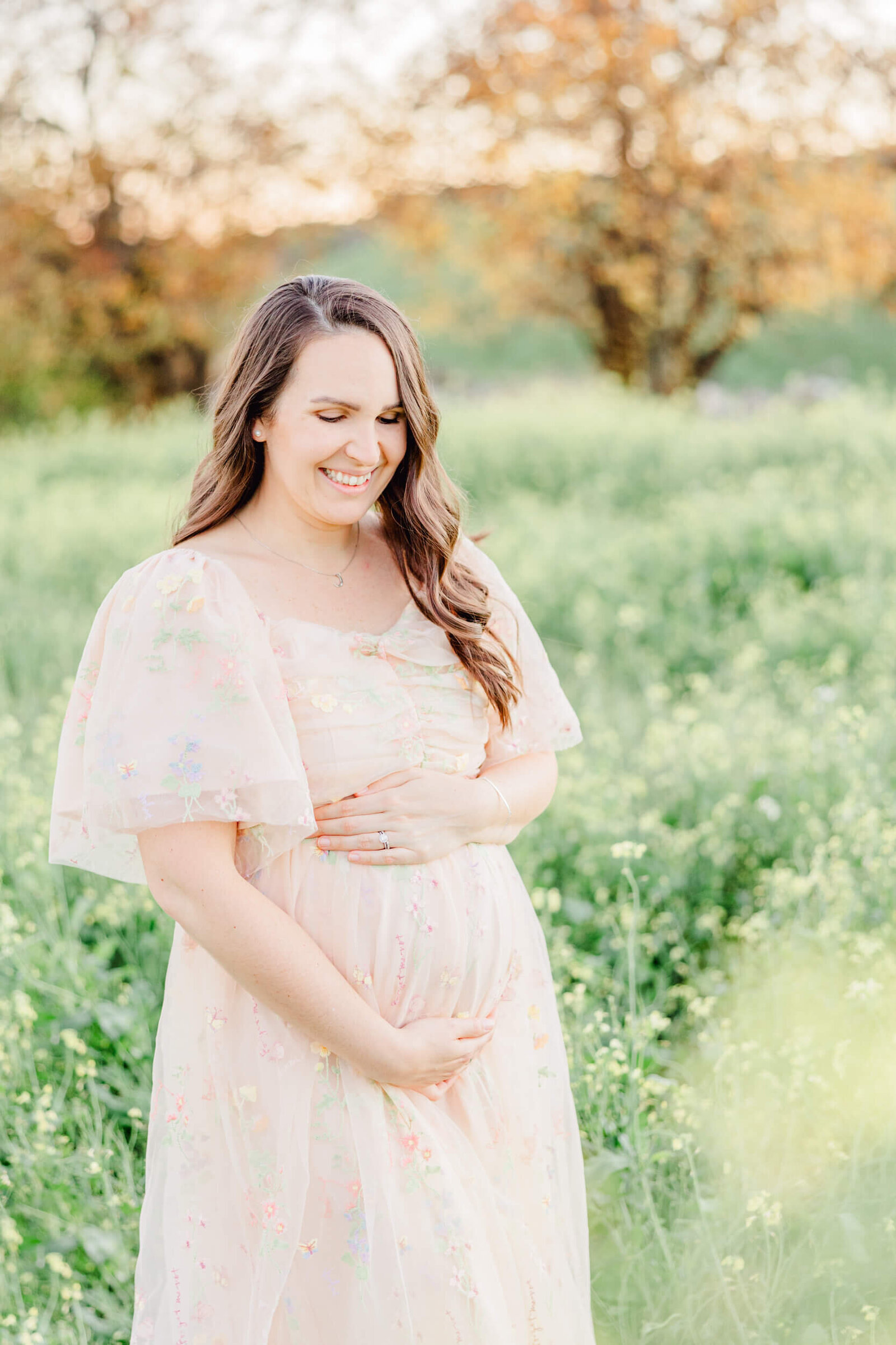 Pregnant woman smiles down at her baby bump in a field of yellow flowers