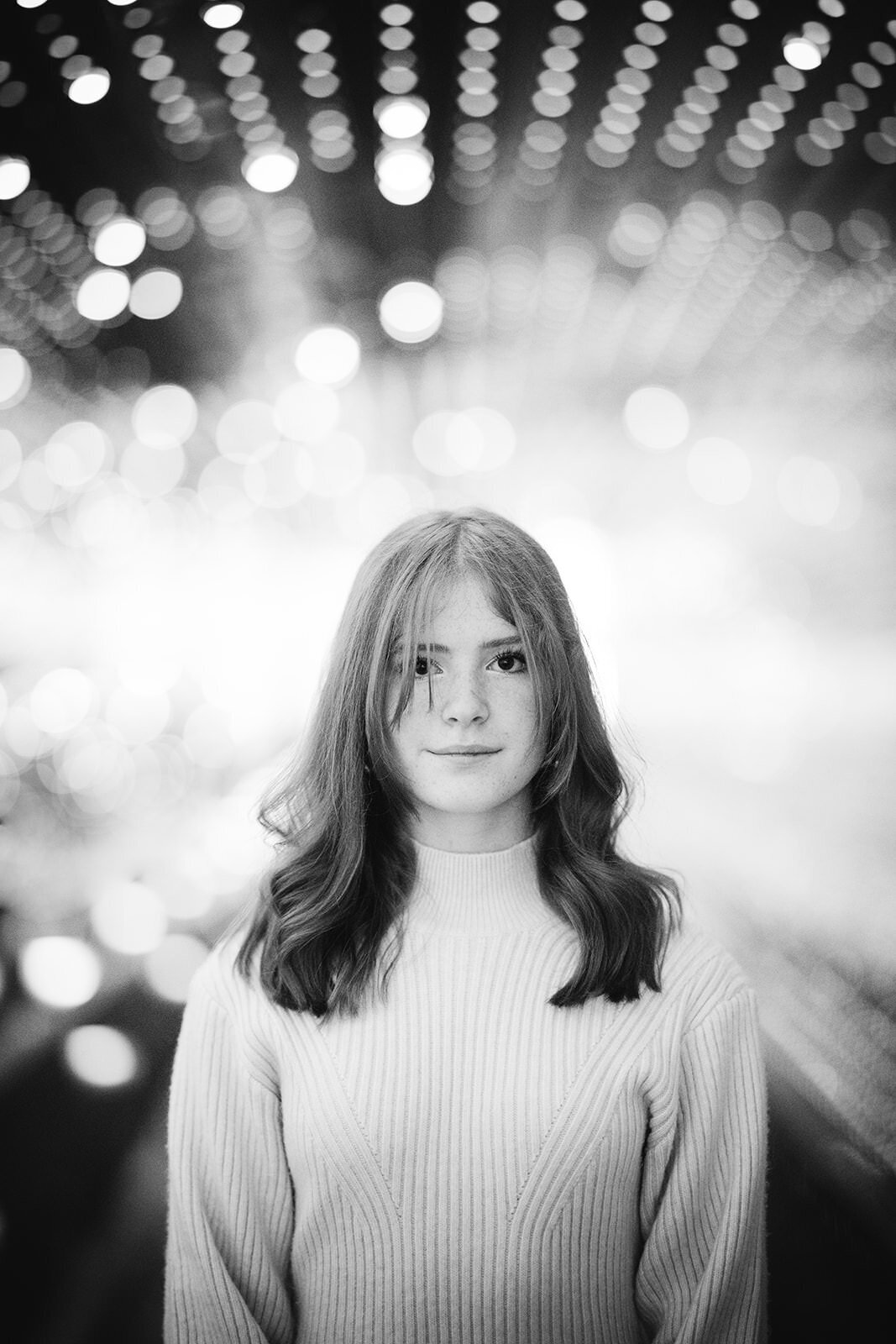 Stylized black-and-white portrait of a red-haired teen standing confidently under a canopy of twinkling lights.