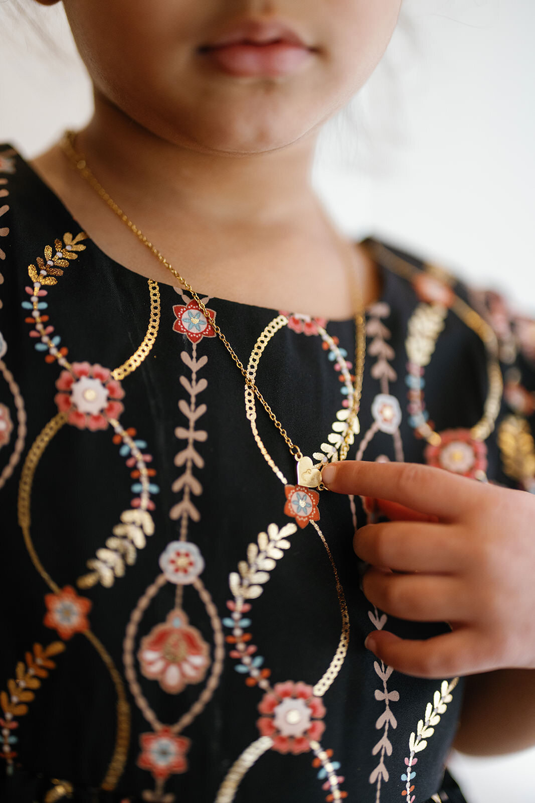 A close-up of a child’s hands gently holding a delicate gold necklace, adorned with intricate floral patterns, emphasizing personal connection and timeless detail.