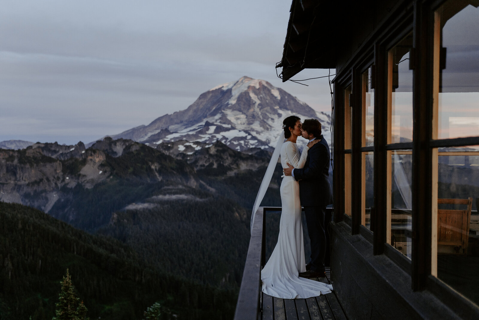 Bride and groom kissing on a fire lookout in front of Mount Rainier at sunset