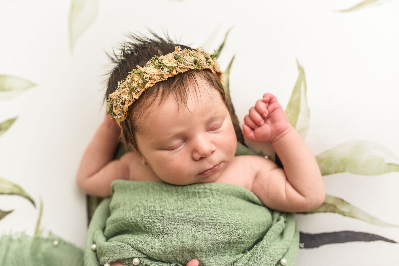 new born baby laying  in white blanket with green plants wrapped in a green blanket