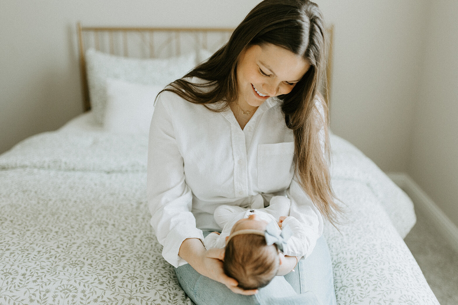 A Lafayette, Indiana newborn and family photographer who captured an image of a new mom sitting on a bed looking down at her newborn baby. 