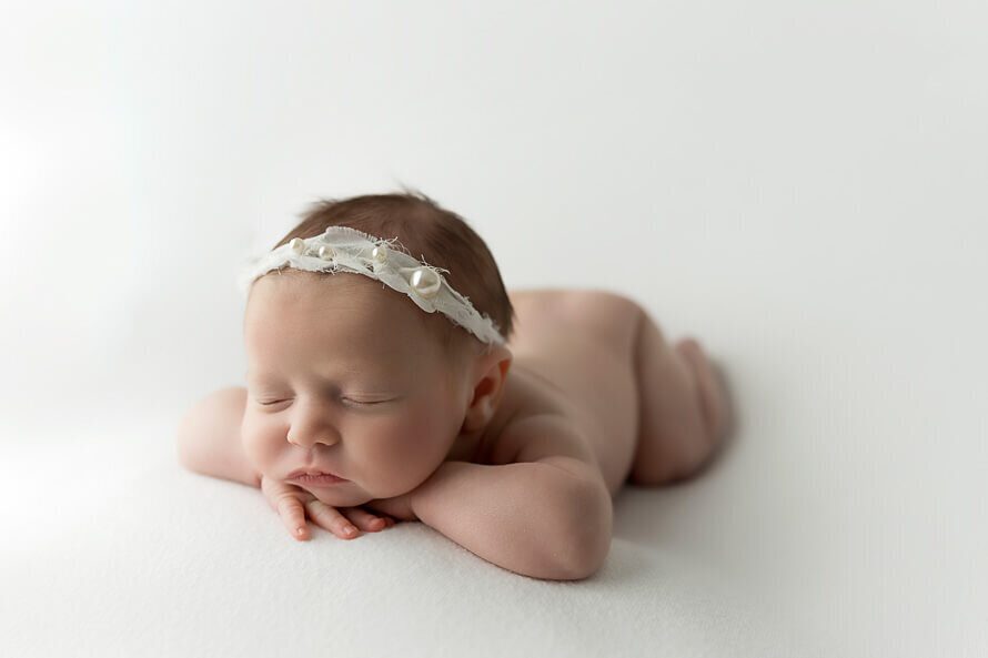 Baby with her head on hands in the white studio at Angela Marie Media.