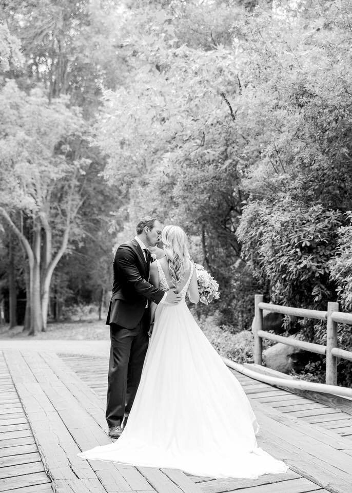 Black and white photo of groom kissing the bride while bride holding a bouquet of flowers