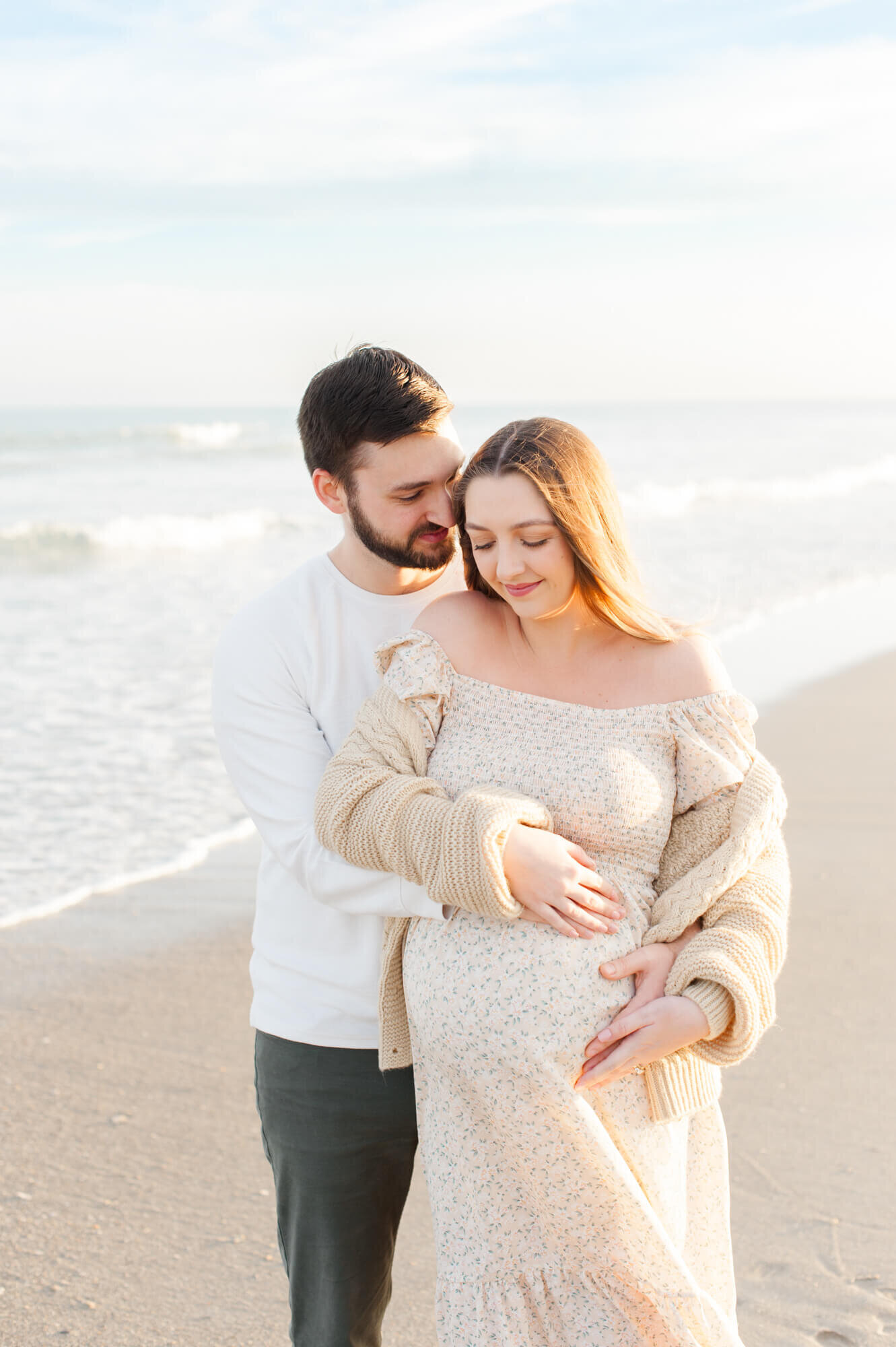 Dad whispers in pregnant moms ear while holding her close on the  beach