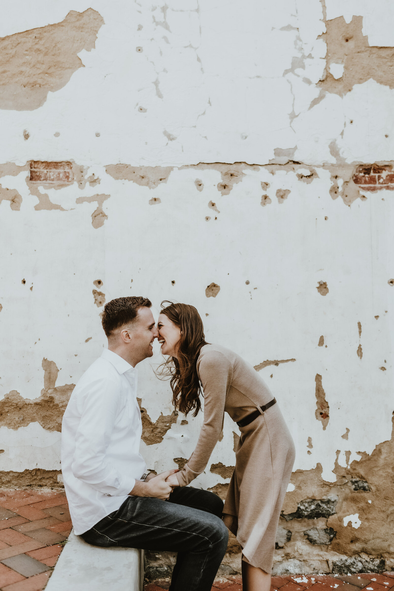 A man sits while a woman stands in front of a vintage wall