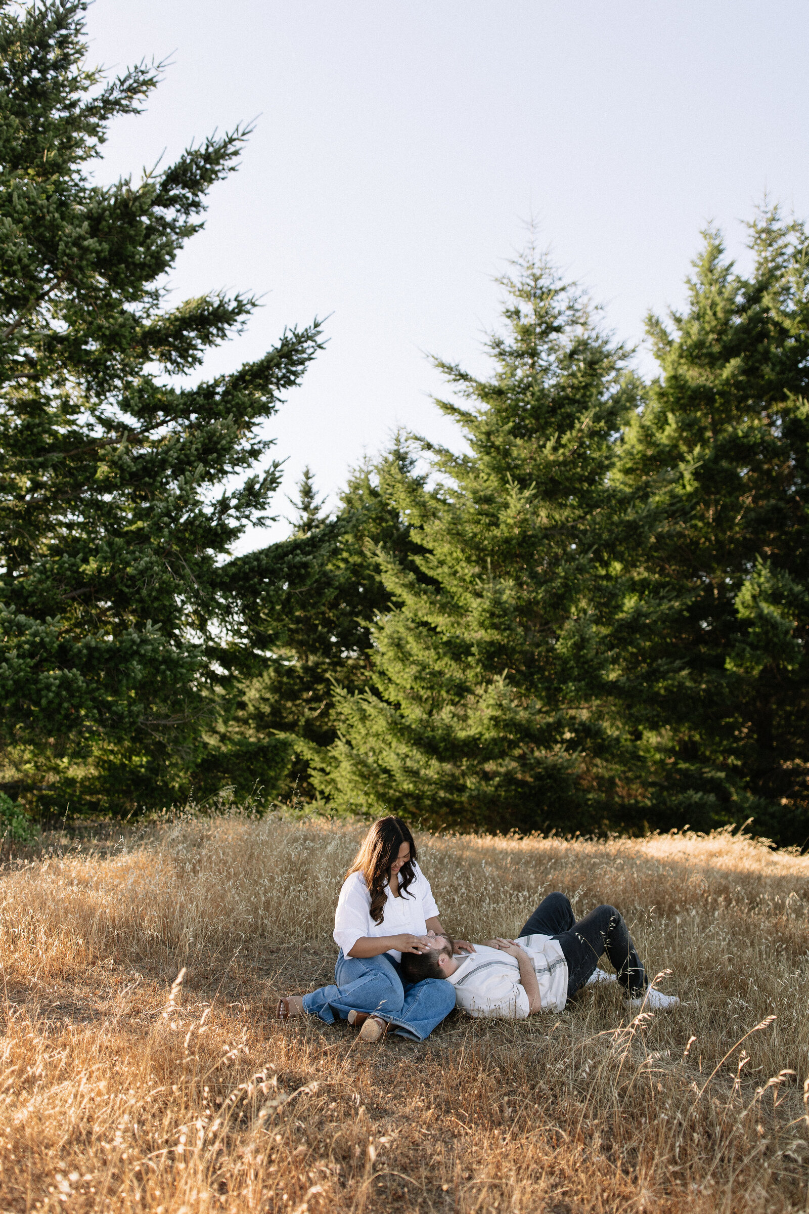 Couple sitting close in tall grass during engagement session in Marin County