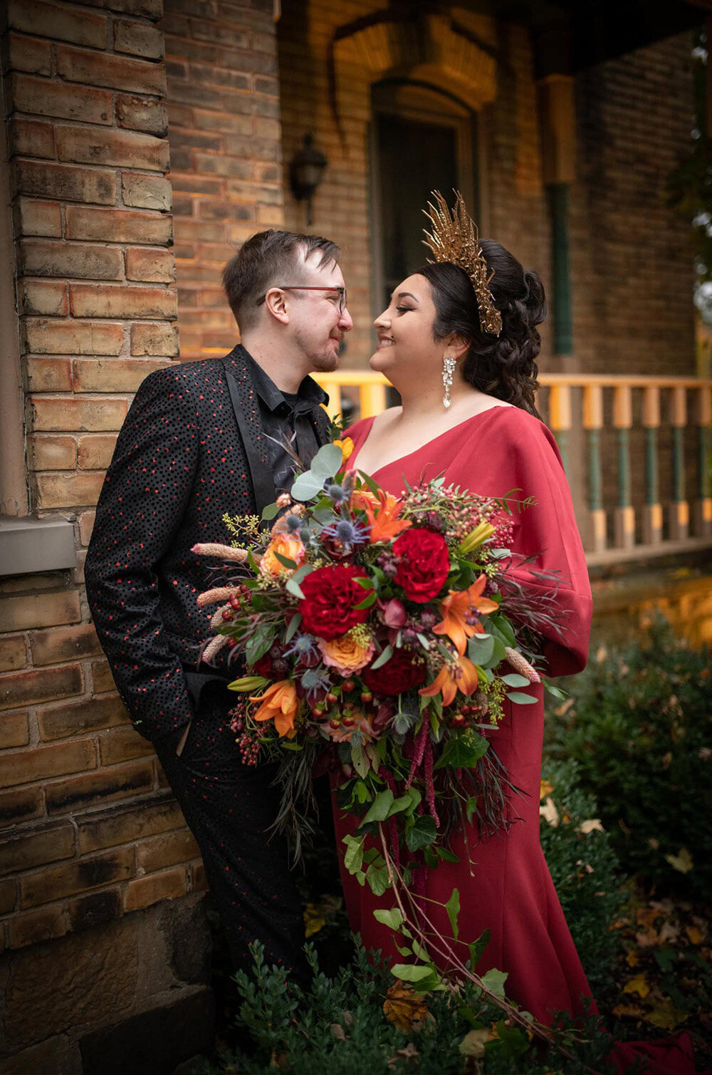 bride in red and groom in black smile behind huge bridal flowers