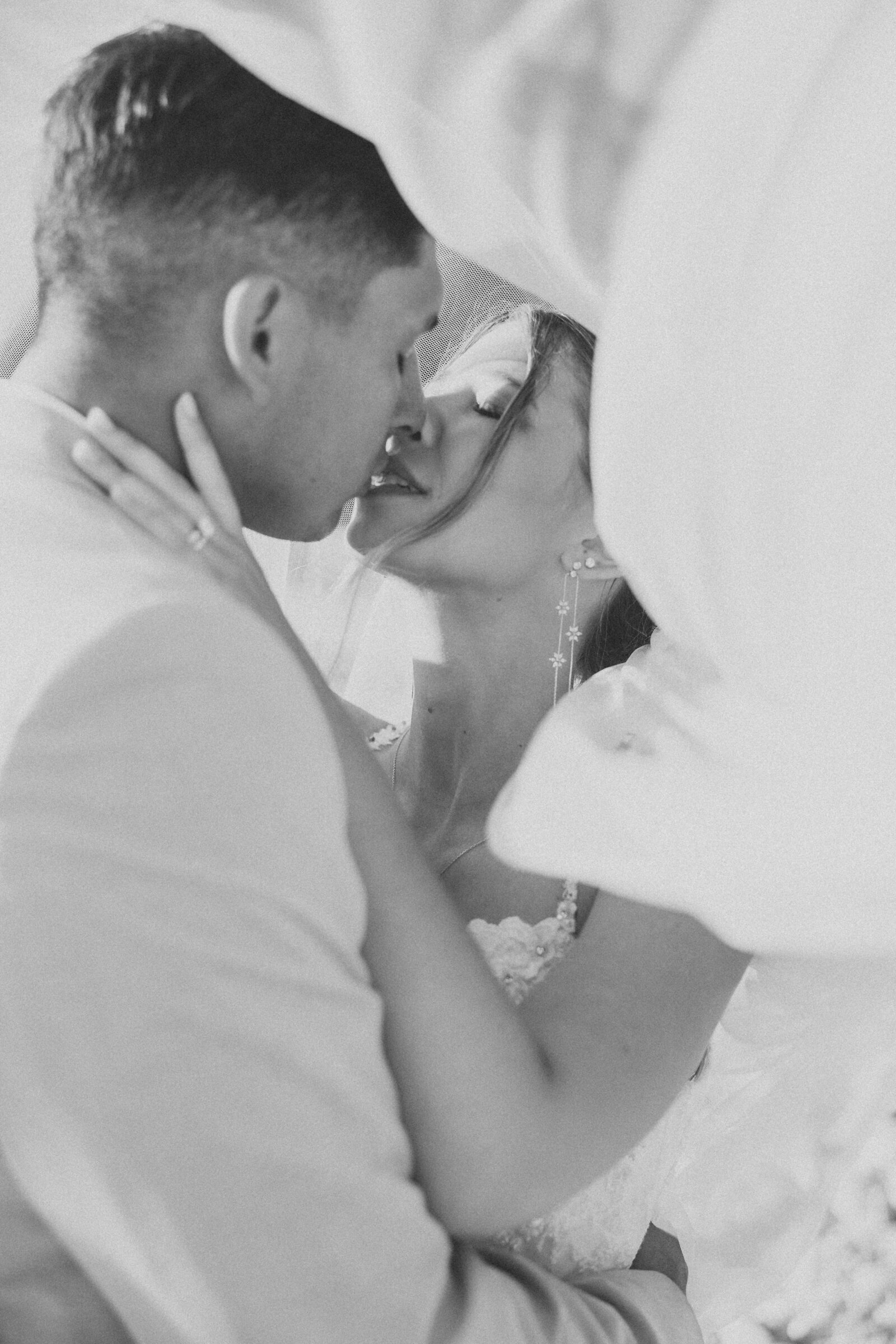 bride and groom kissing underneath a veil