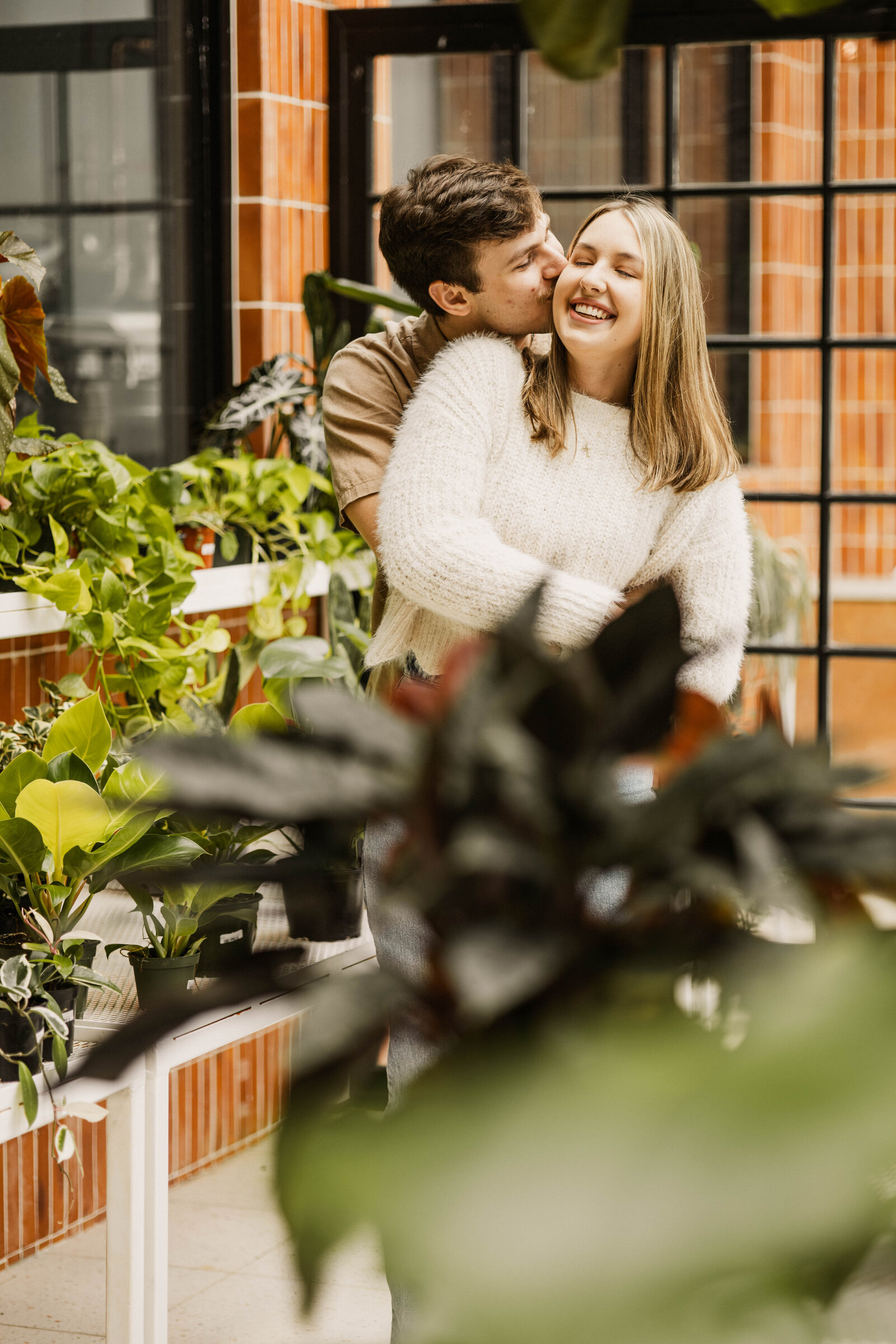 Luke kissing Megan's cheek during their engagement session in a greenhouse next door to Comeback Coffee in Memphis.