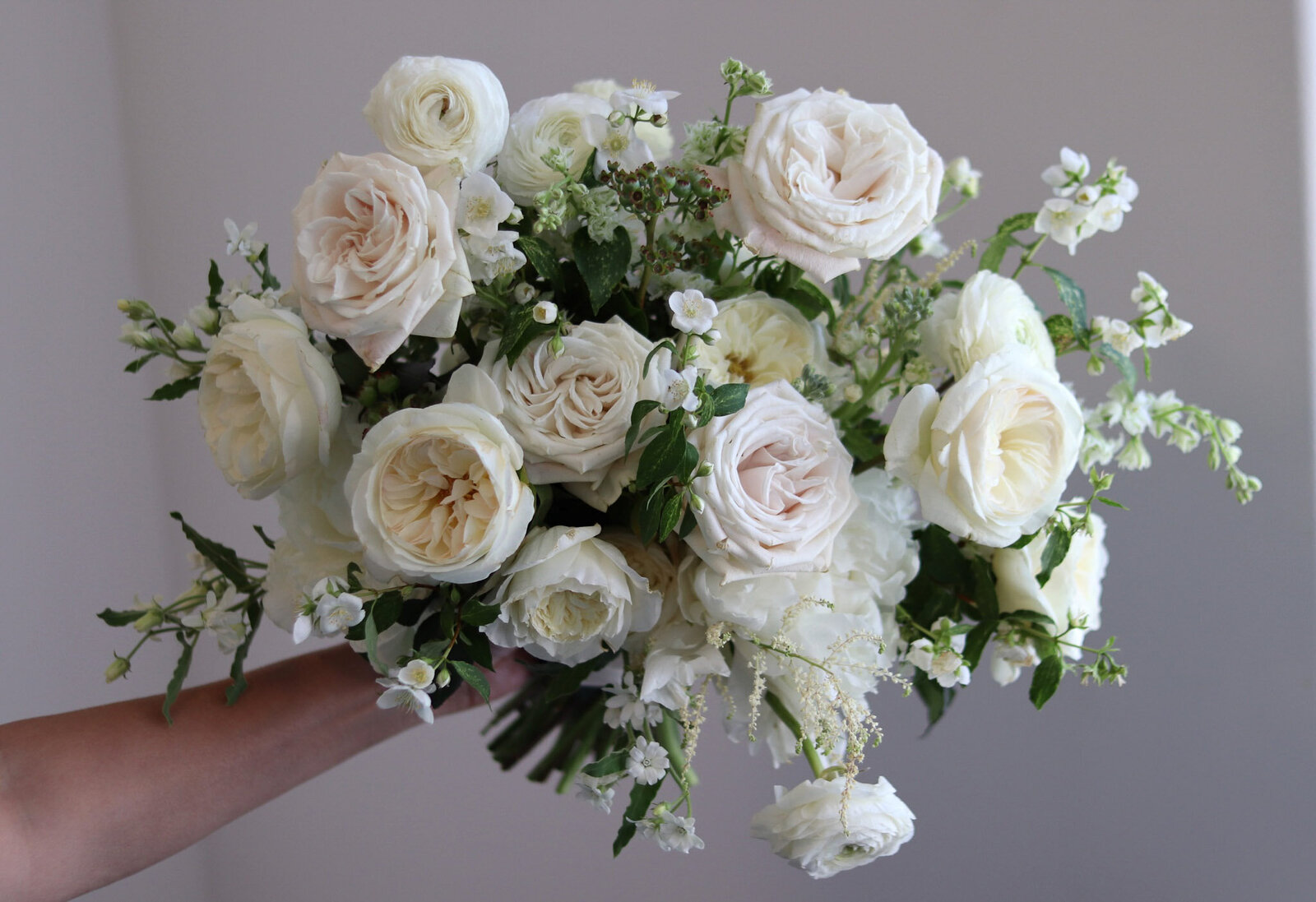 Beautiful white bridal bouquet with roses, ranunculus, mock orange, astilbe, blueberry foliage, and peonies.