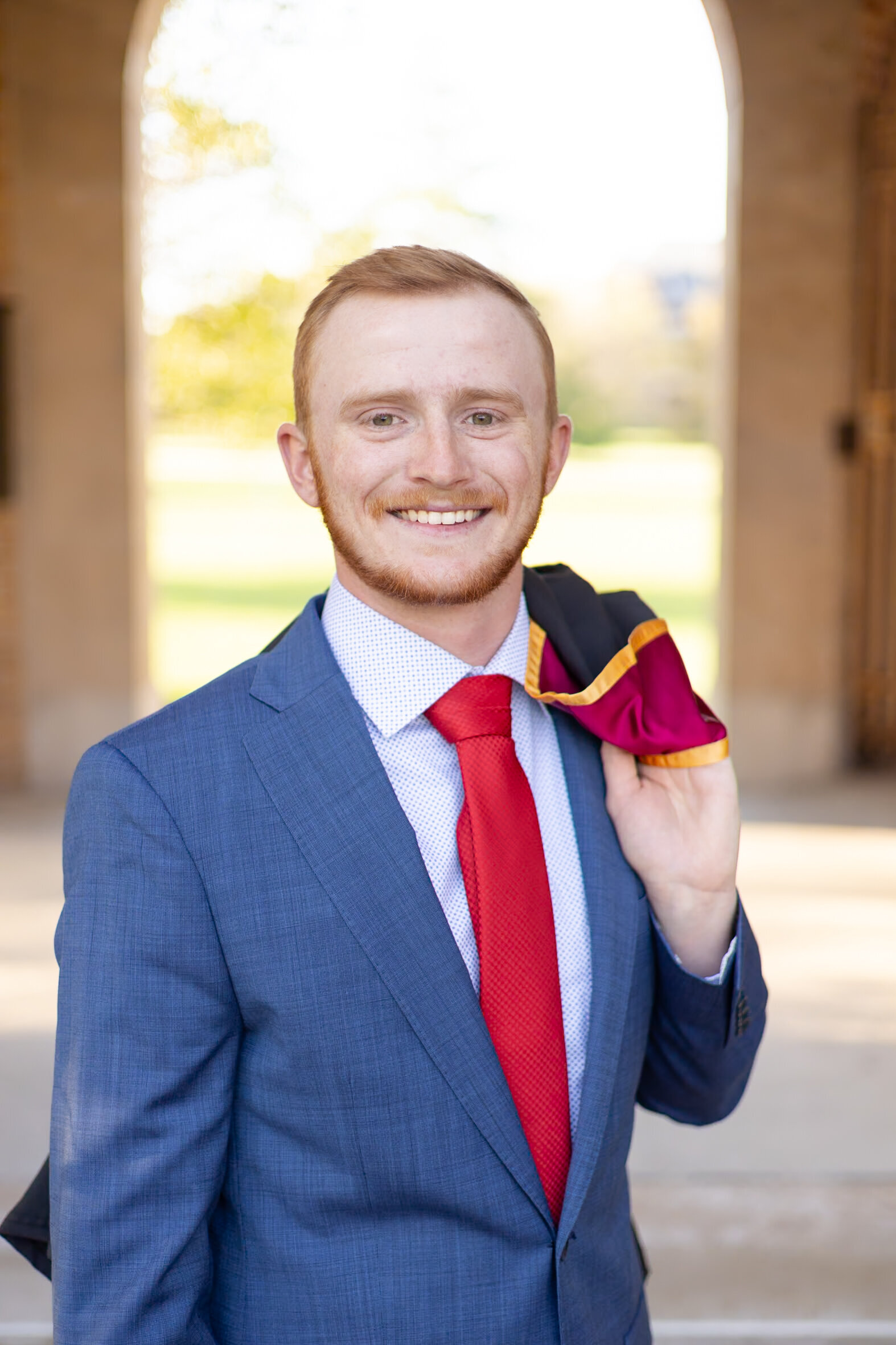 young man poses for cap and gown photo in front of Iowa State Campanile