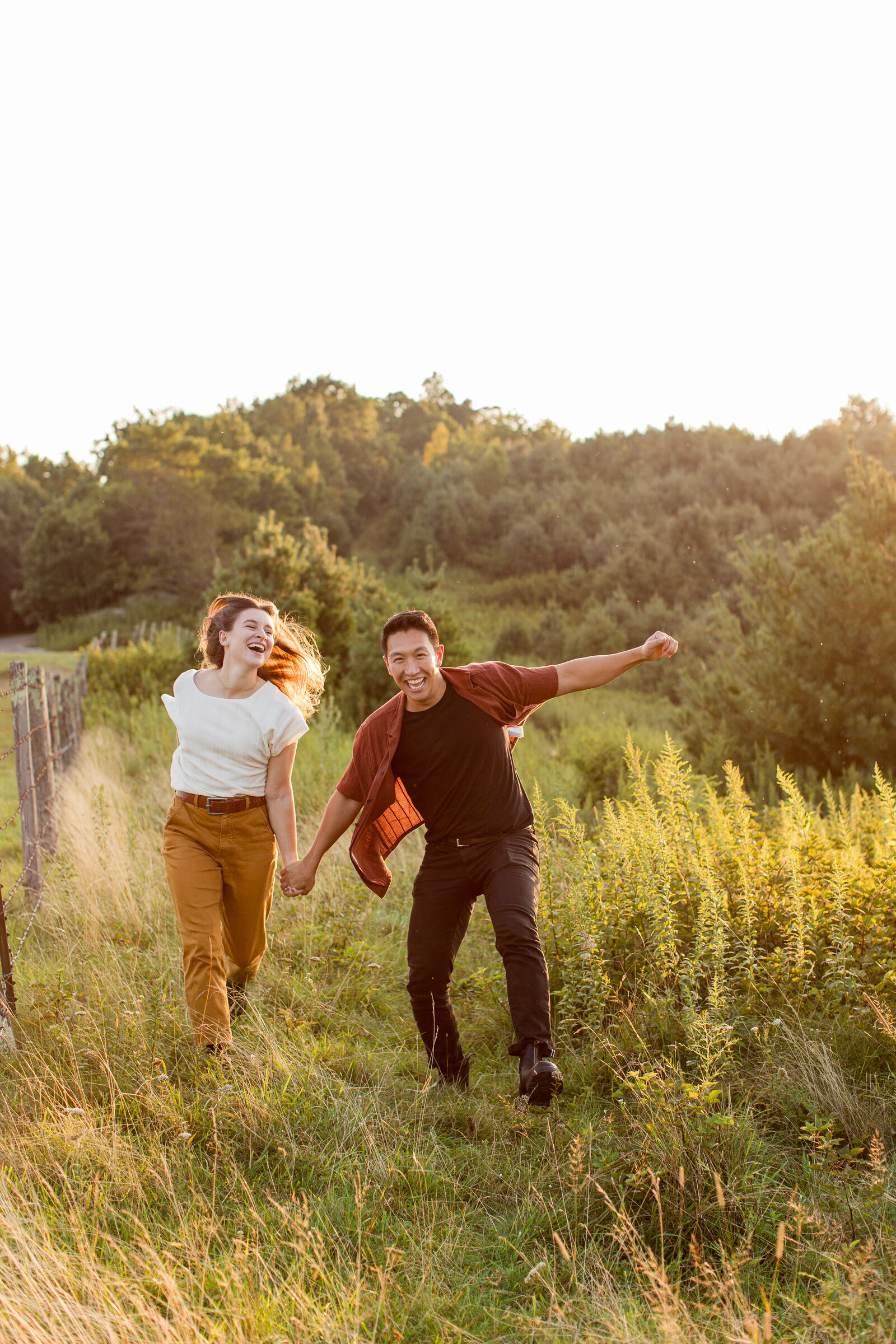 Engagement photos of a couple skipping through a field at sunset during their Boone, NC engagement session