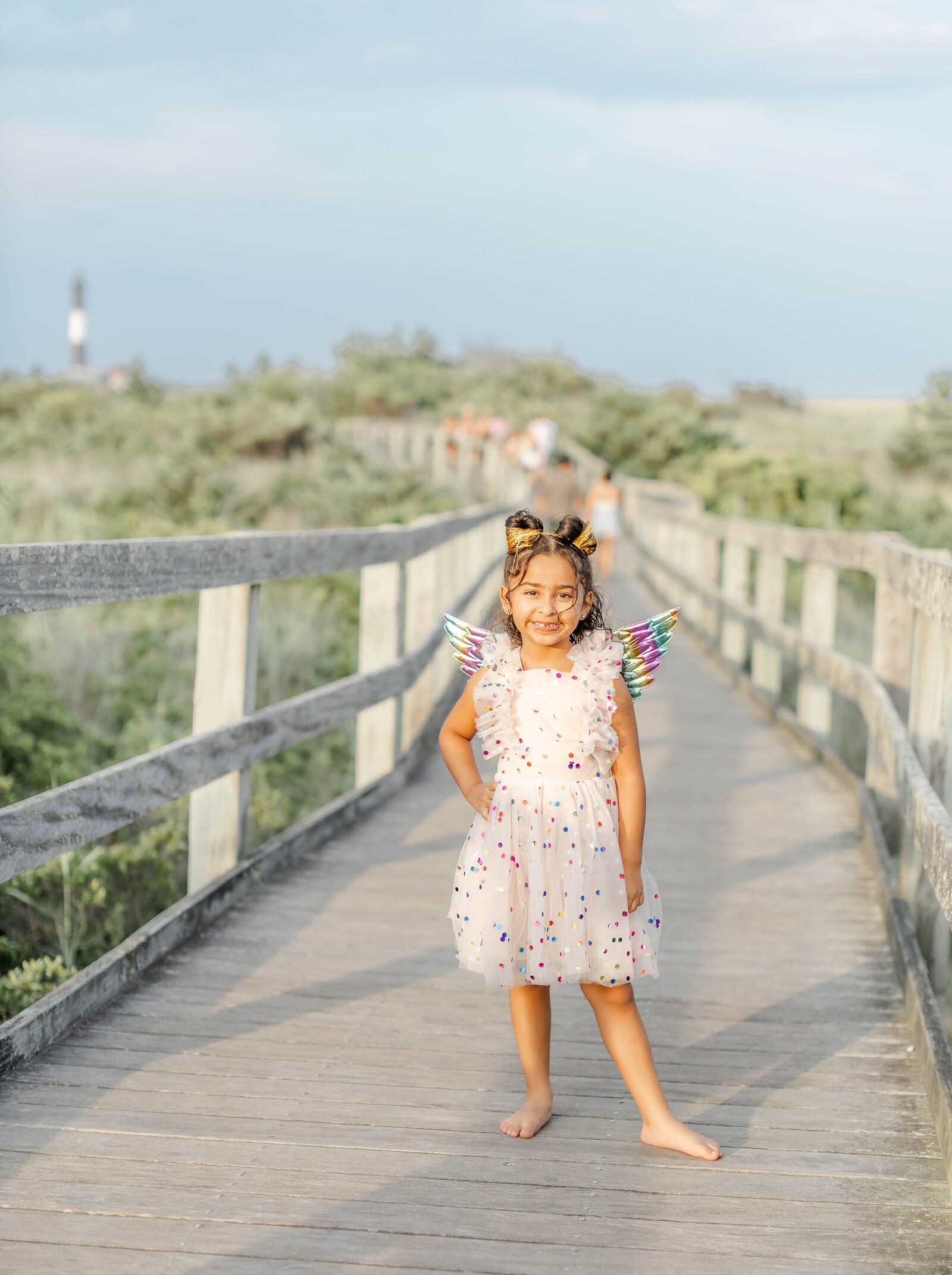 6-year-old girl in a festive dress smiling on a wooden boardwalk at sunset during her Long Island birthday photoshoot.
