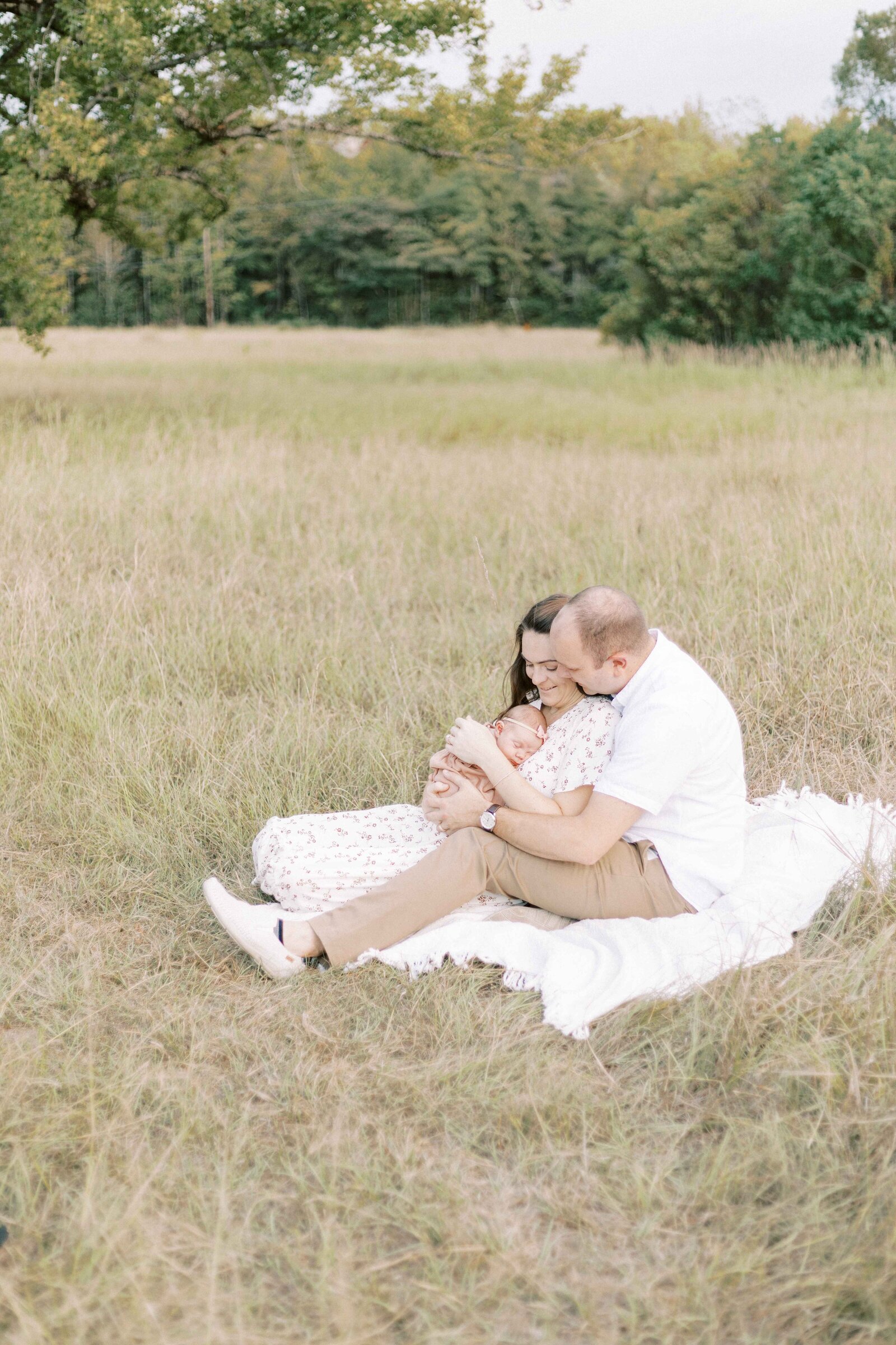 new parents sitting in field with baby in peoria illinois newborn photos 