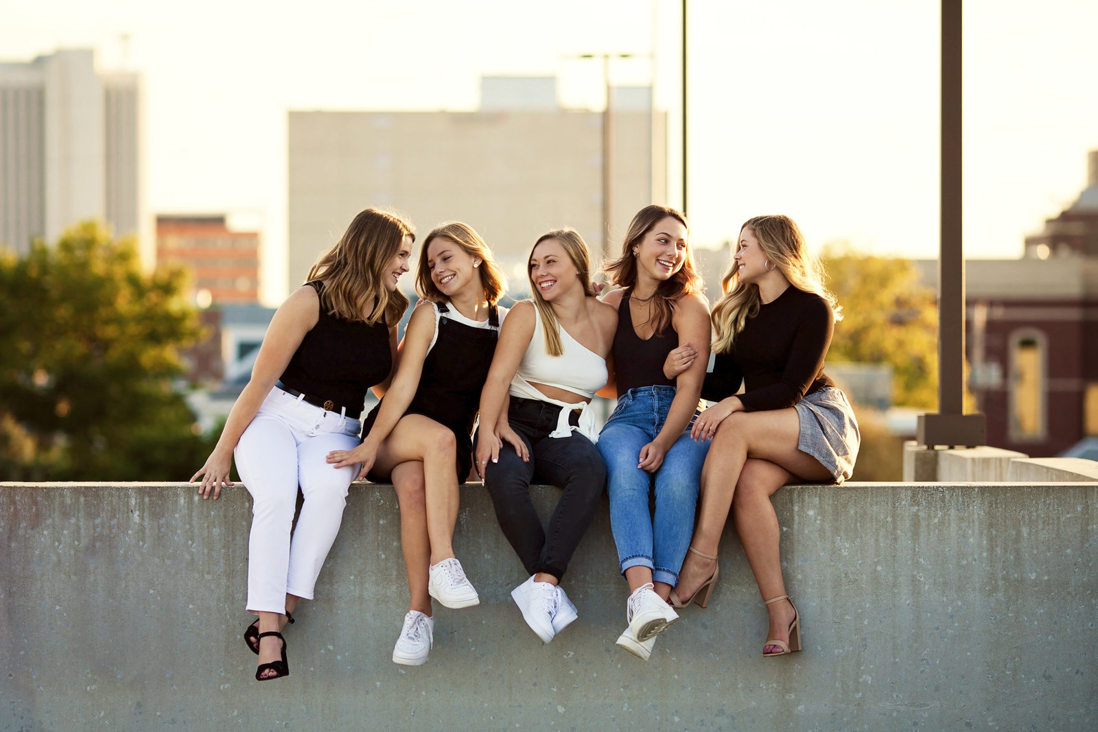 Five senior girls sitting atop a parking ramp smiling at each other.