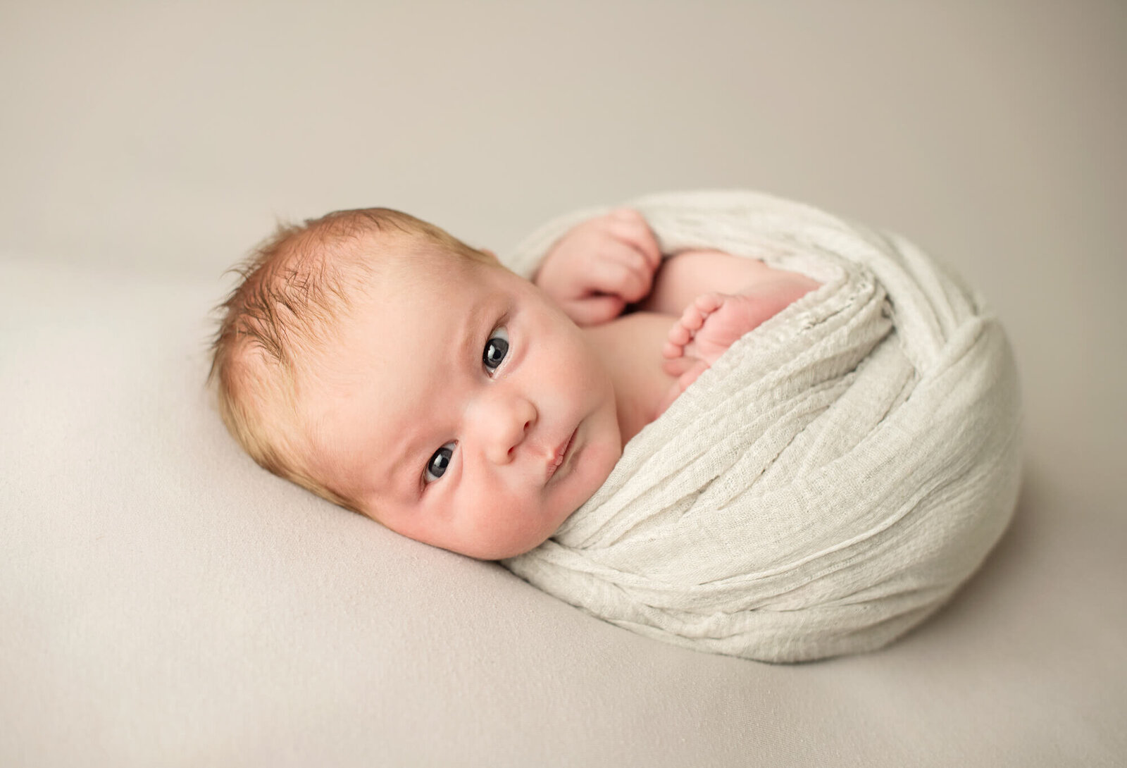 Awake newborn boy with cream wrap