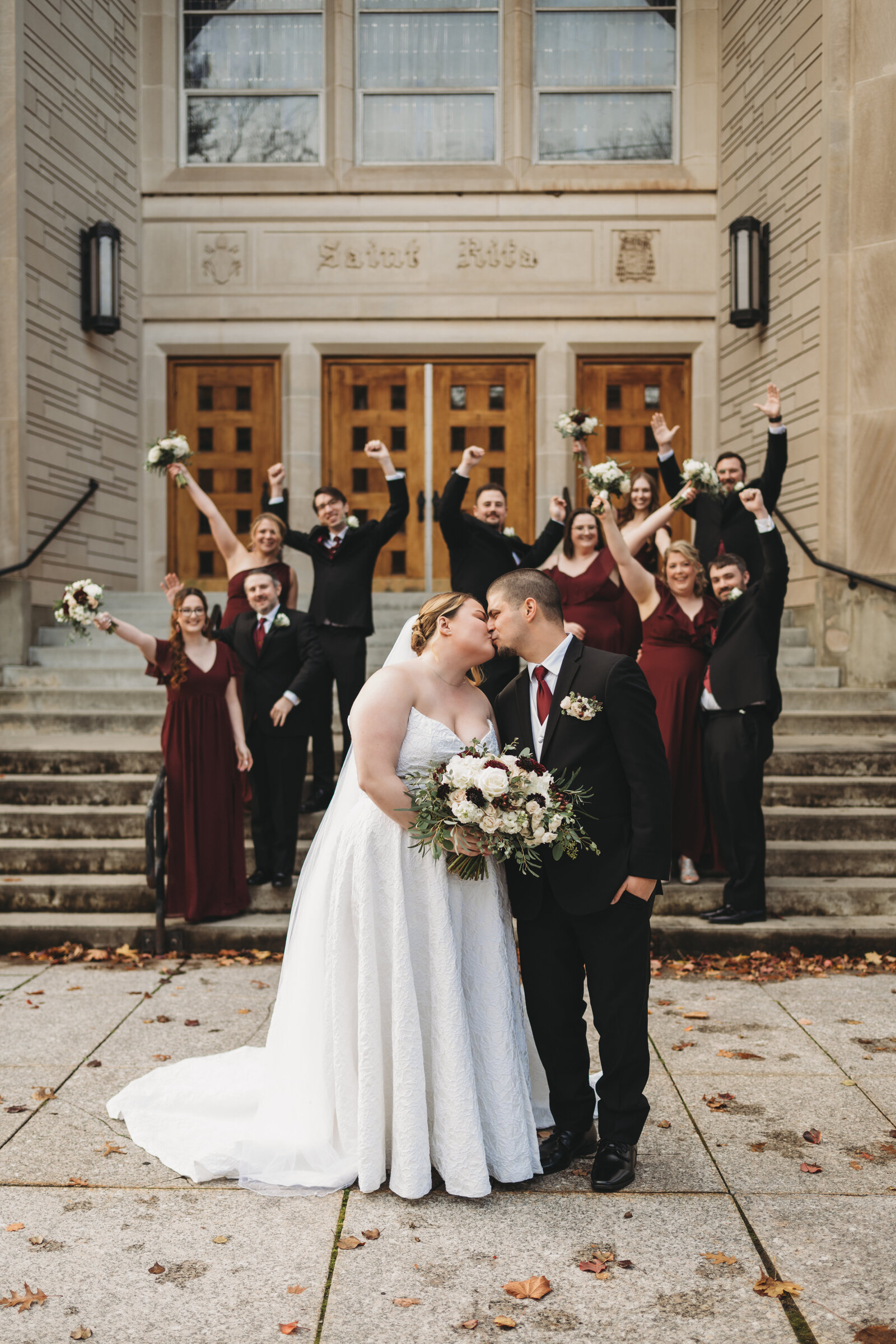 A newlywed couple shares a romantic kiss in front of their cheering wedding party, celebrating their love on the steps of a grand venue. Capturing the joy, excitement, and timeless elegance of a Connecticut wedding, this image is perfect for couples looking for wedding photography inspiration.