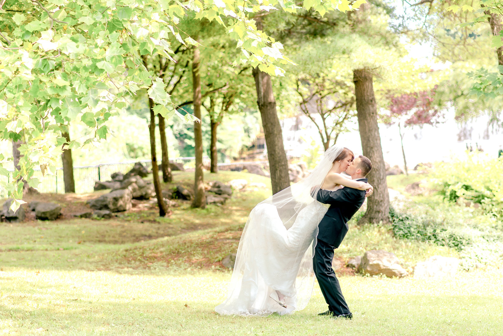 Groom lifts his bride for a photo  among light green trees