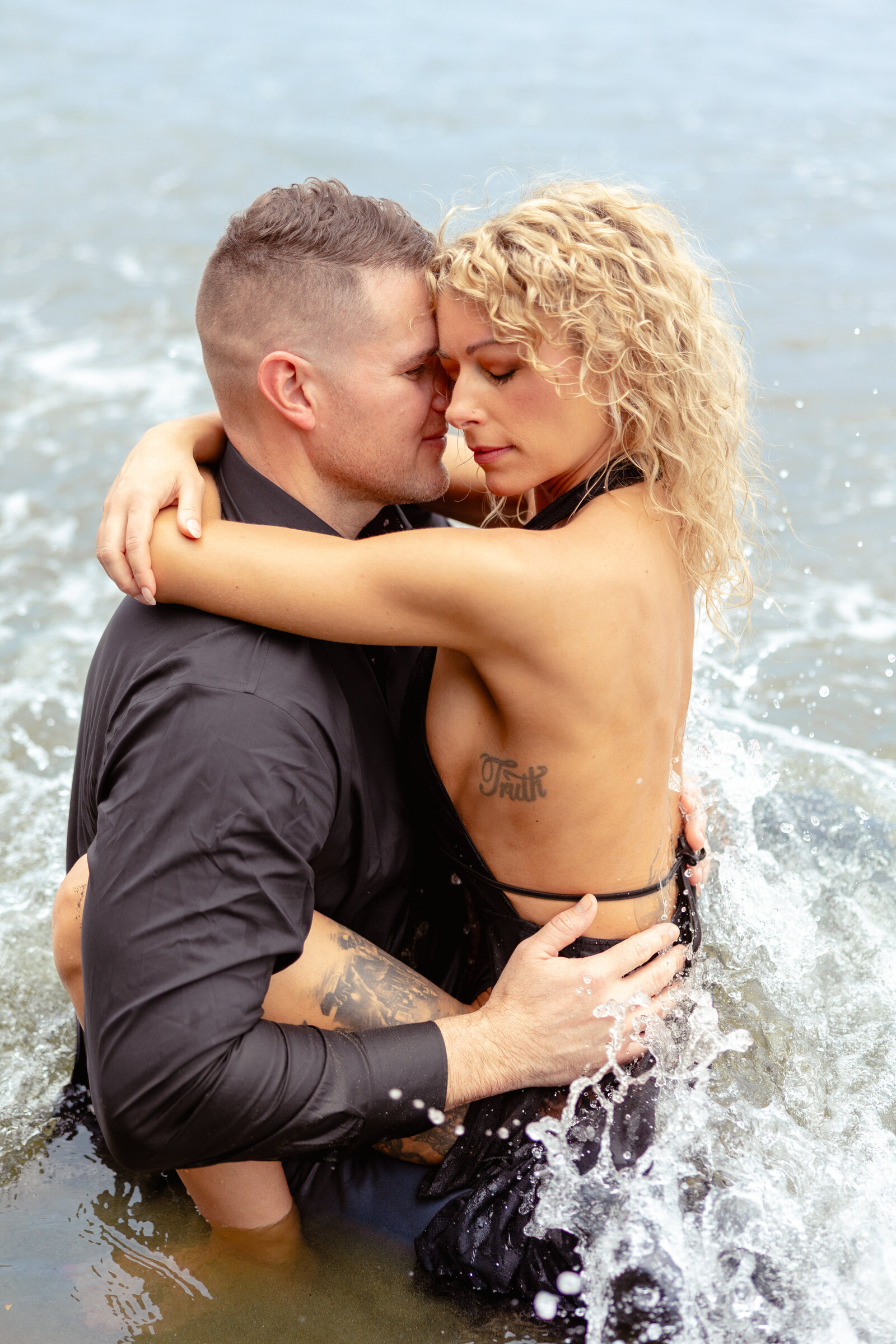 couple embraces as the ocean waves crash around them on the beach